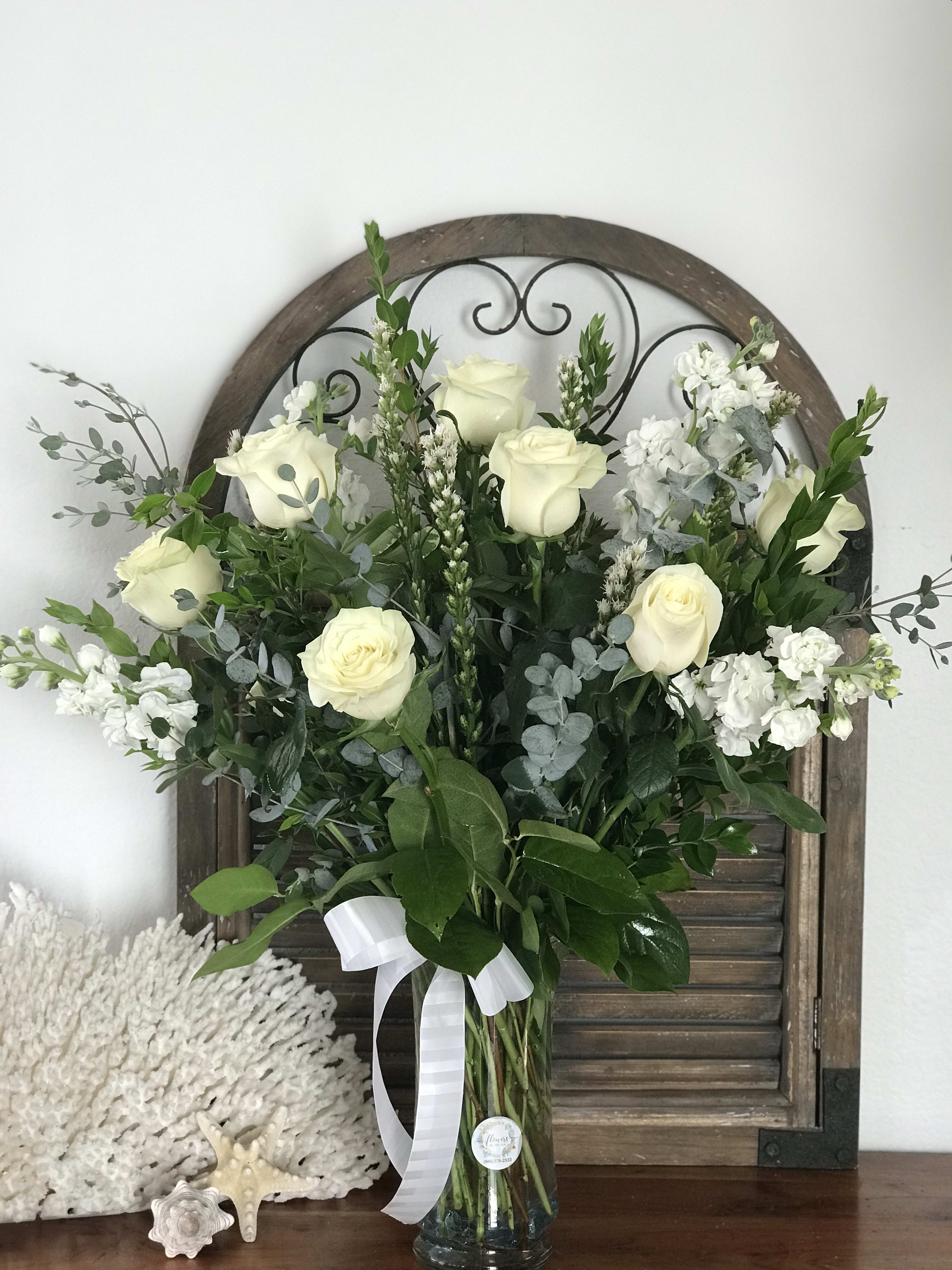 White roses and white filler flowers in a glass vase with greenery