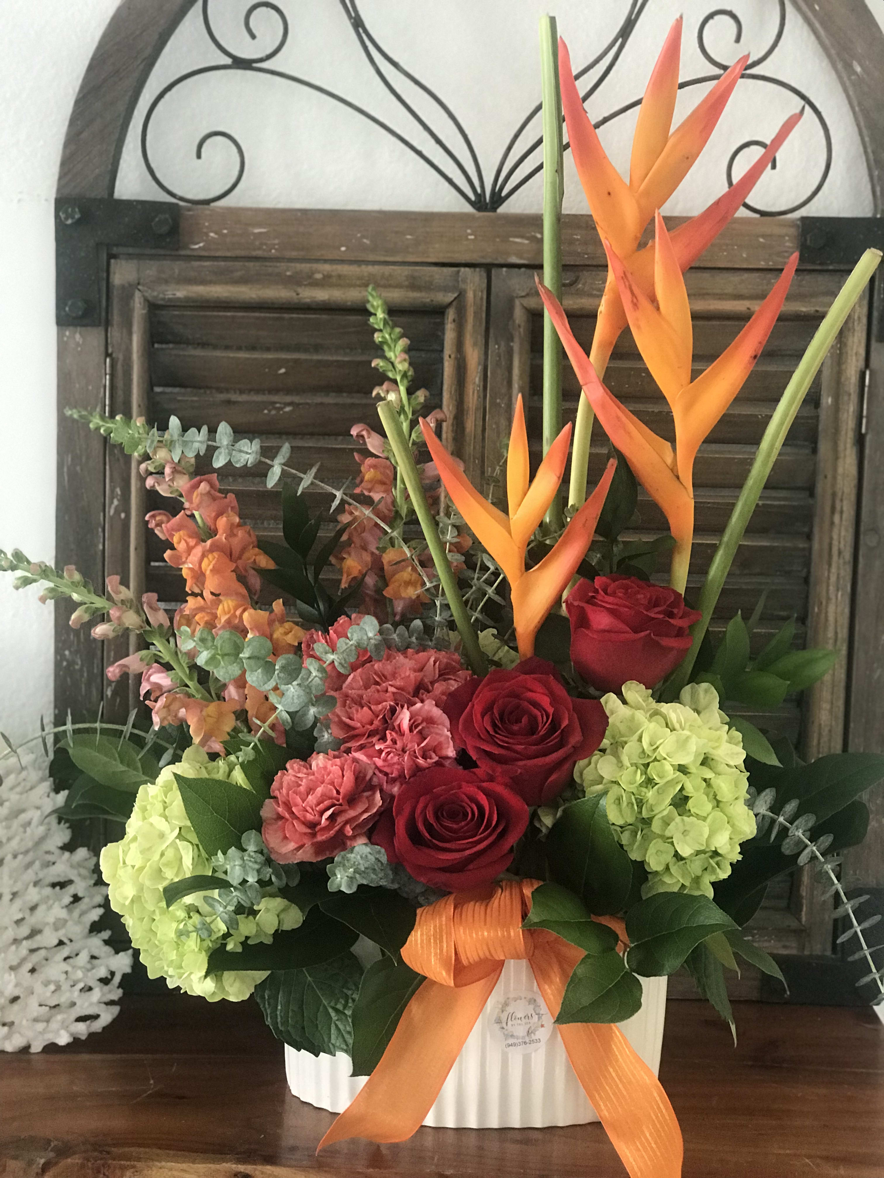 Tropical floral arrangement with red roses, hydrangeas, and orange bird-of-paradise in a white container