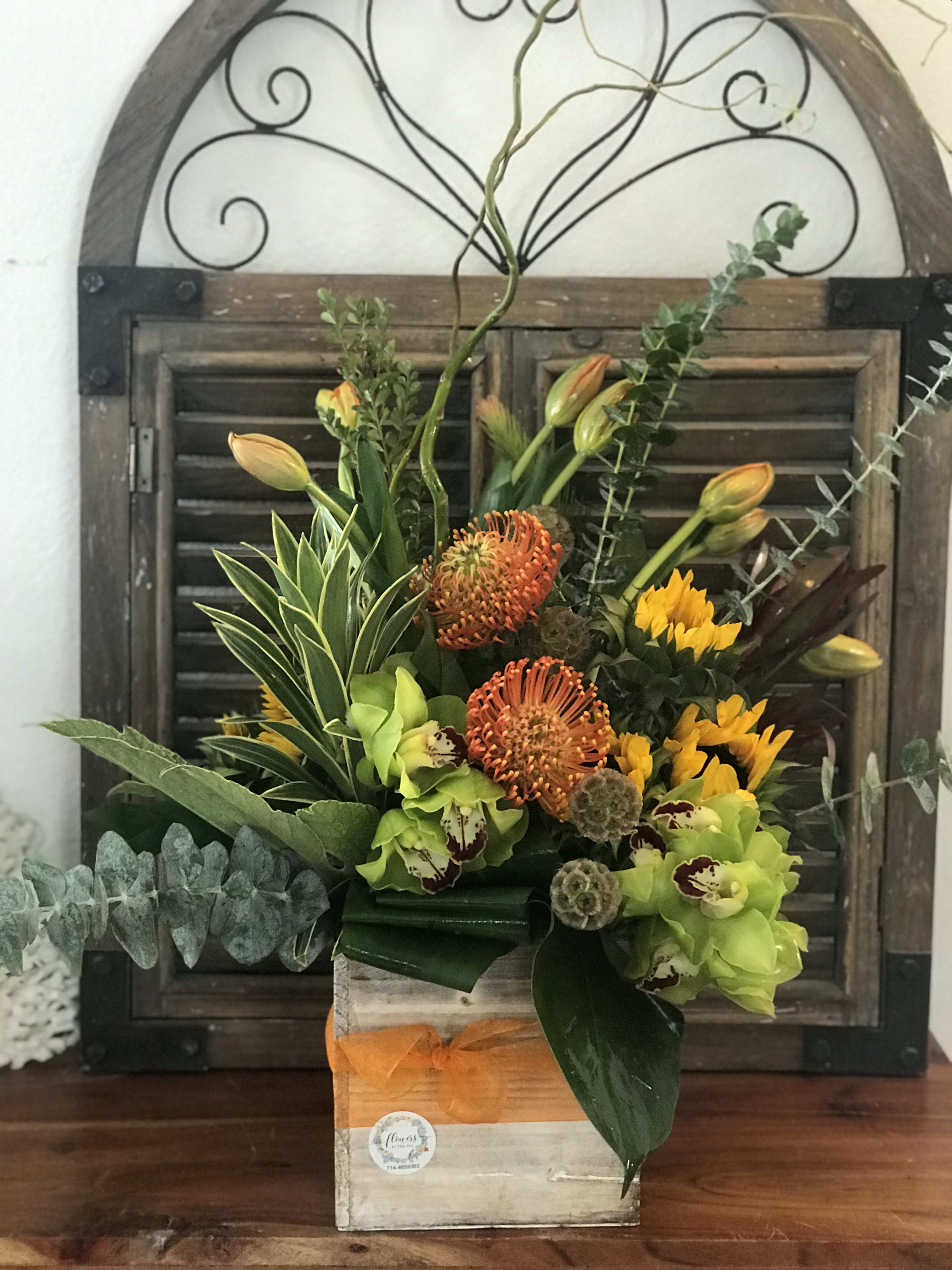 Tropical floral arrangement in a wooden box with orange and green blooms