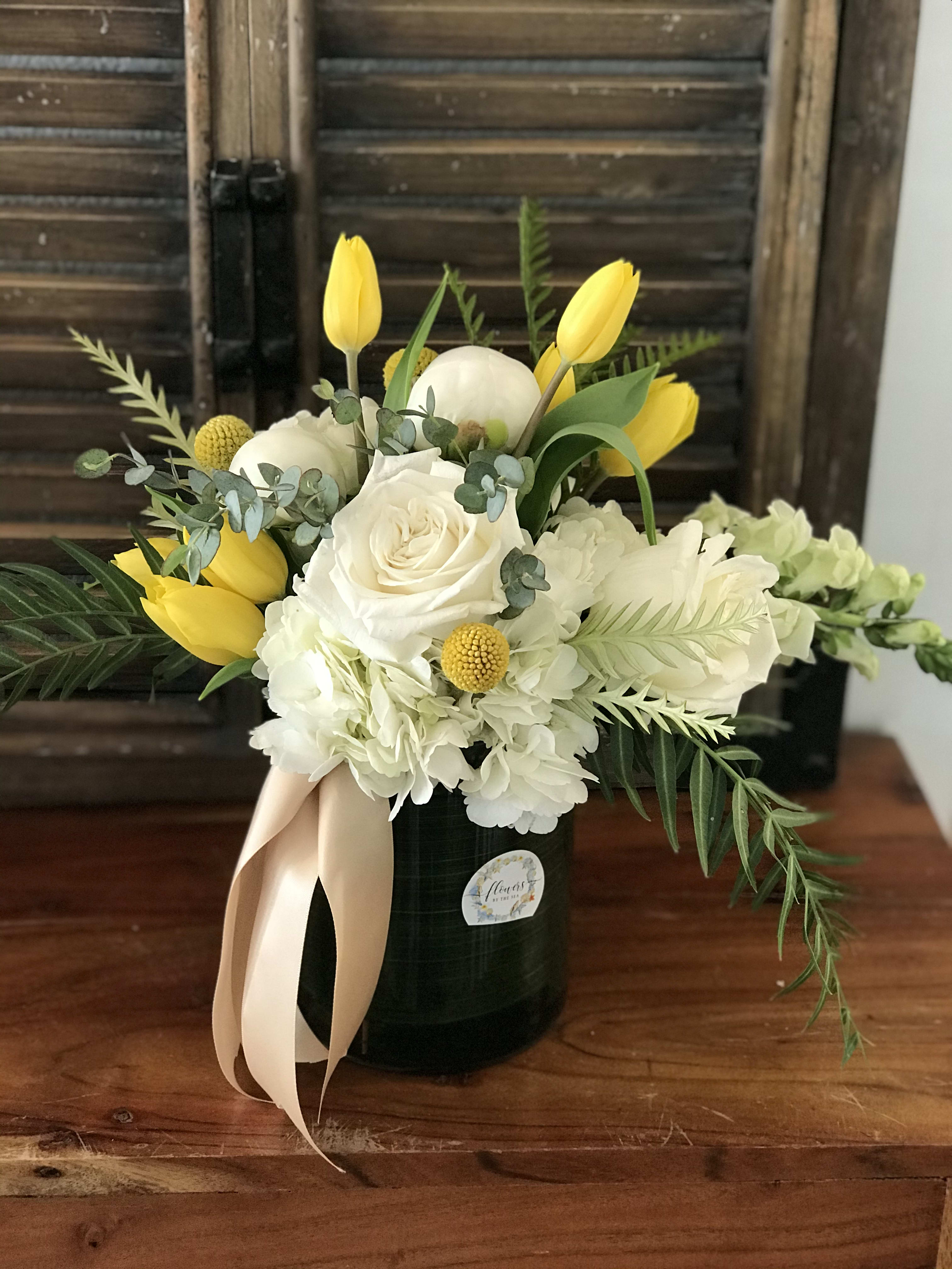 White roses and hydrangeas with yellow tulips in a black vase