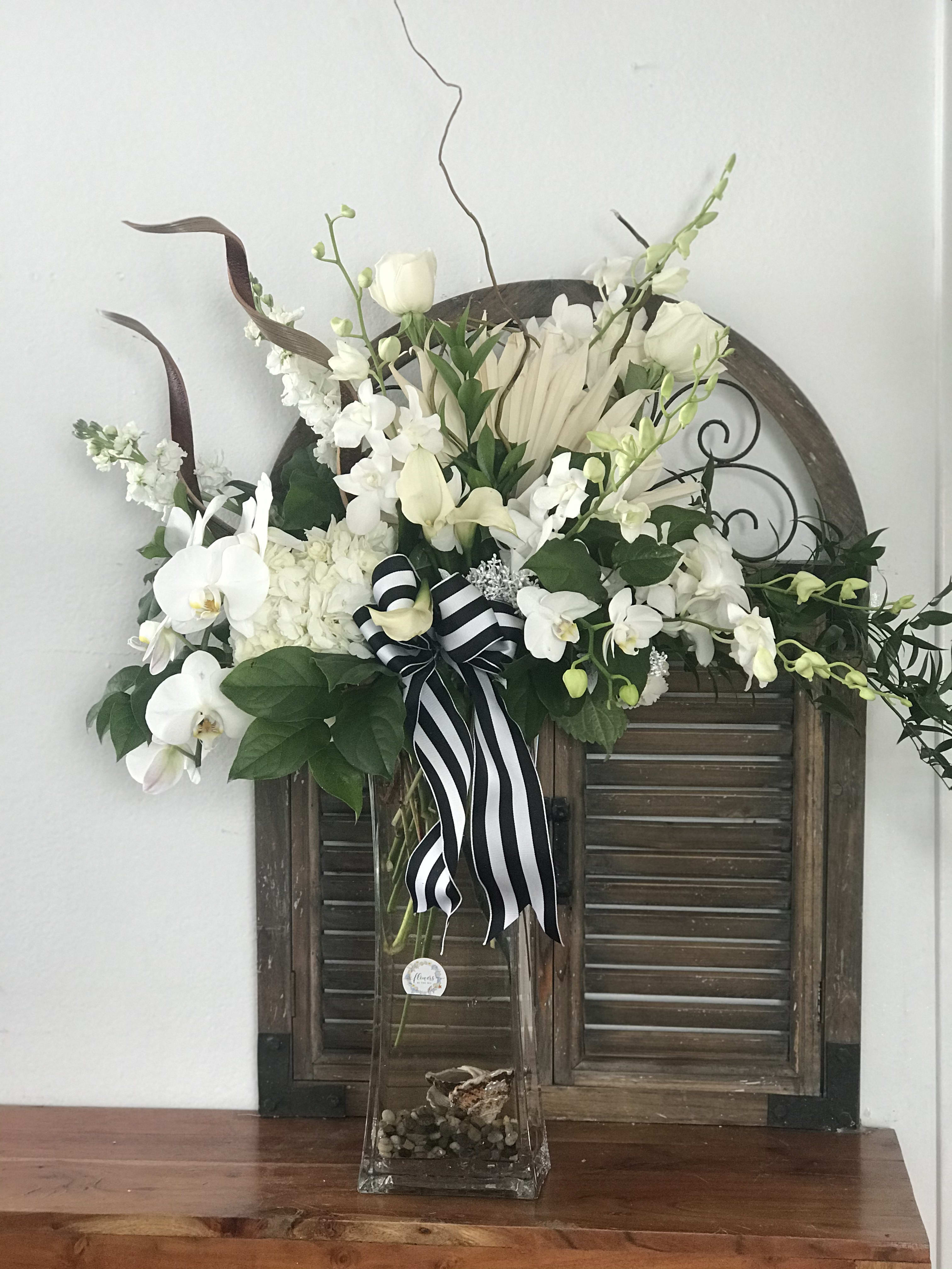 White orchid and rose arrangement in a tall glass vase with a striped ribbon