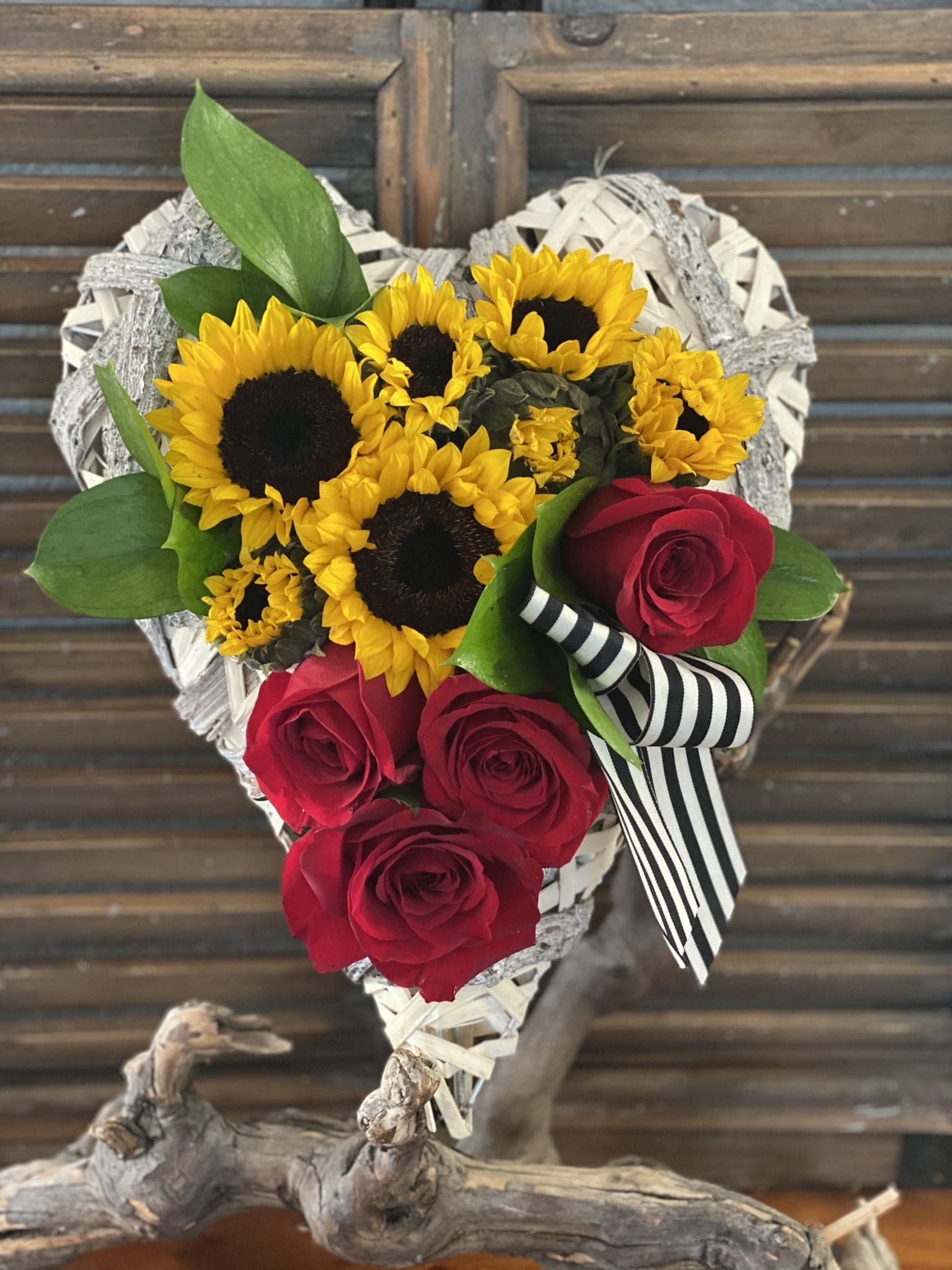 Heart-shaped bouquet of sunflowers and red roses with a striped ribbon