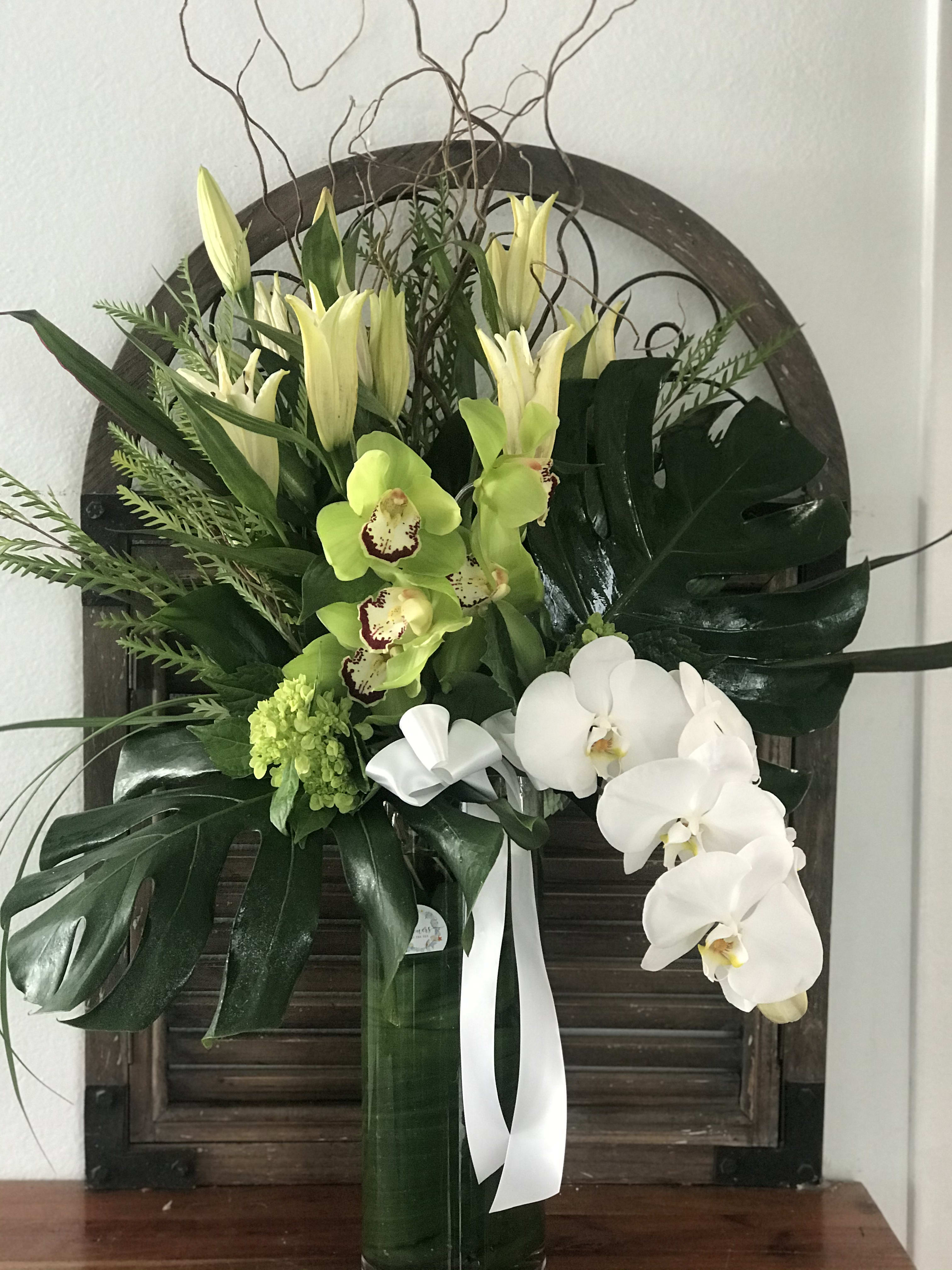 Tall floral arrangement with white orchids and green lilies in a vase