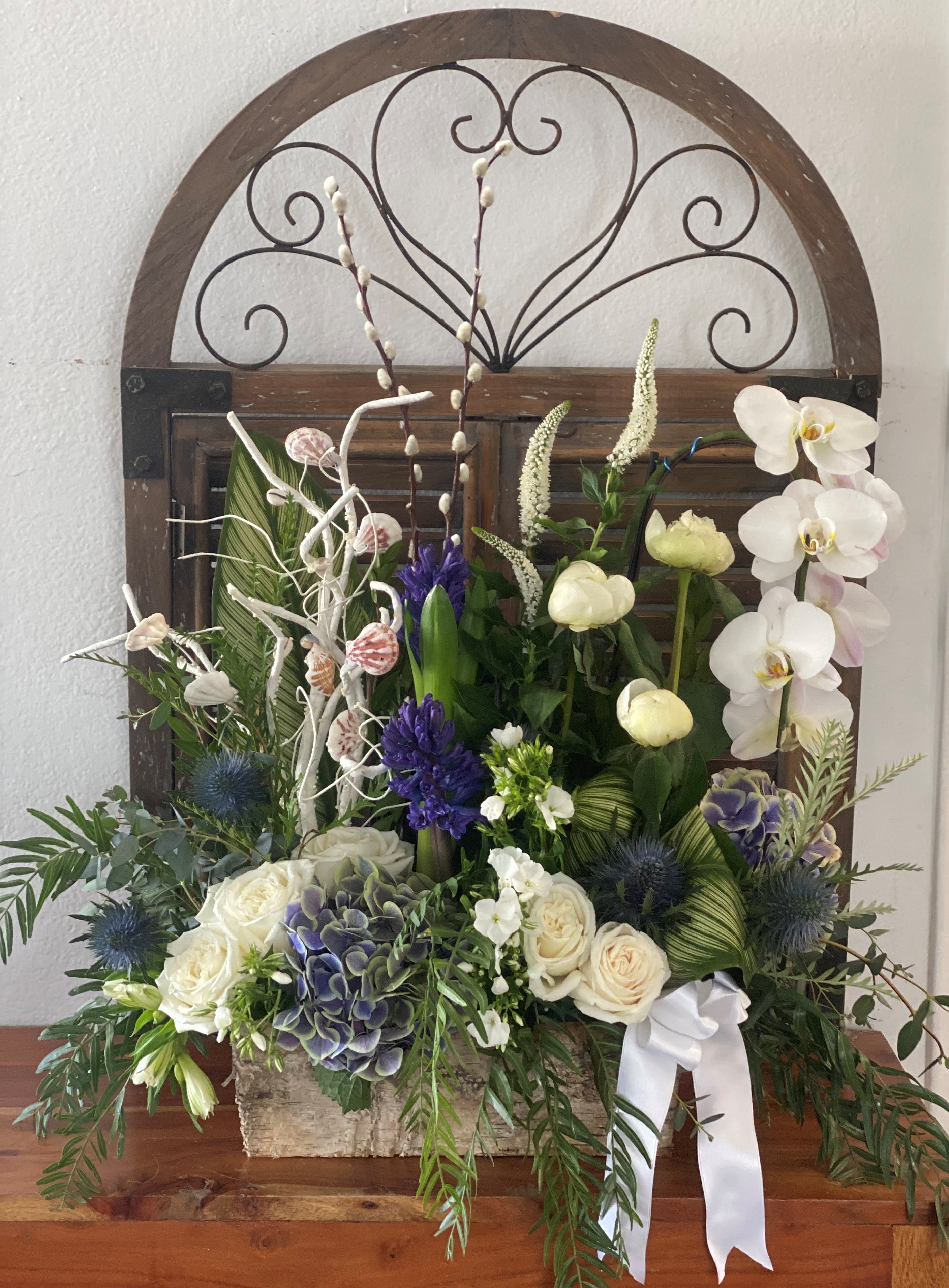 Mixed floral arrangement with white orchids, roses, and blue thistles in a wooden container