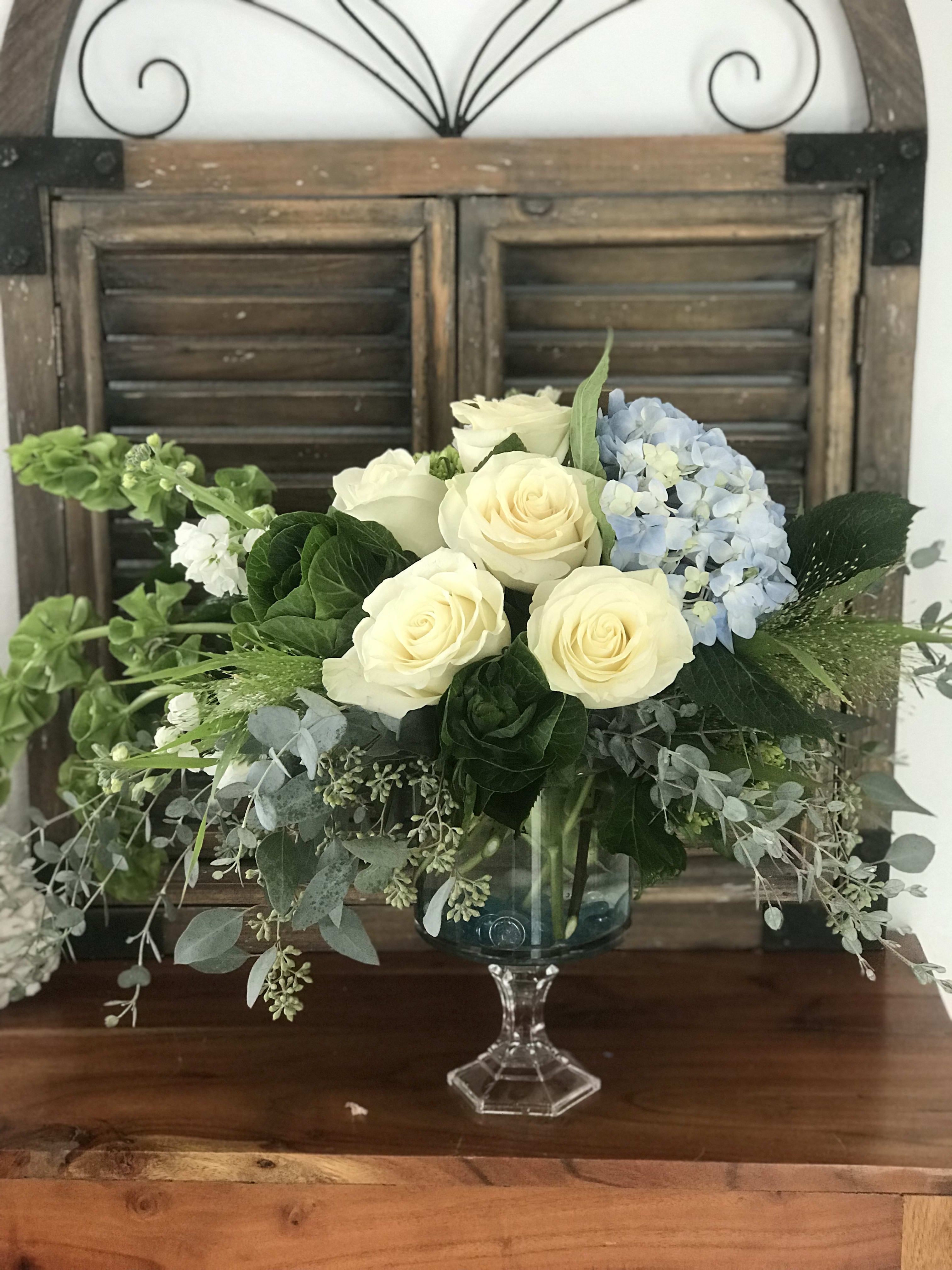 Cream roses and blue hydrangea in a glass pedestal vase
