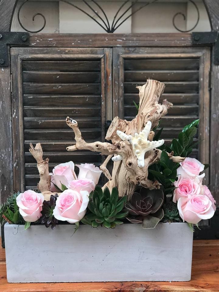 Pink roses and succulents arranged with driftwood in a white planter