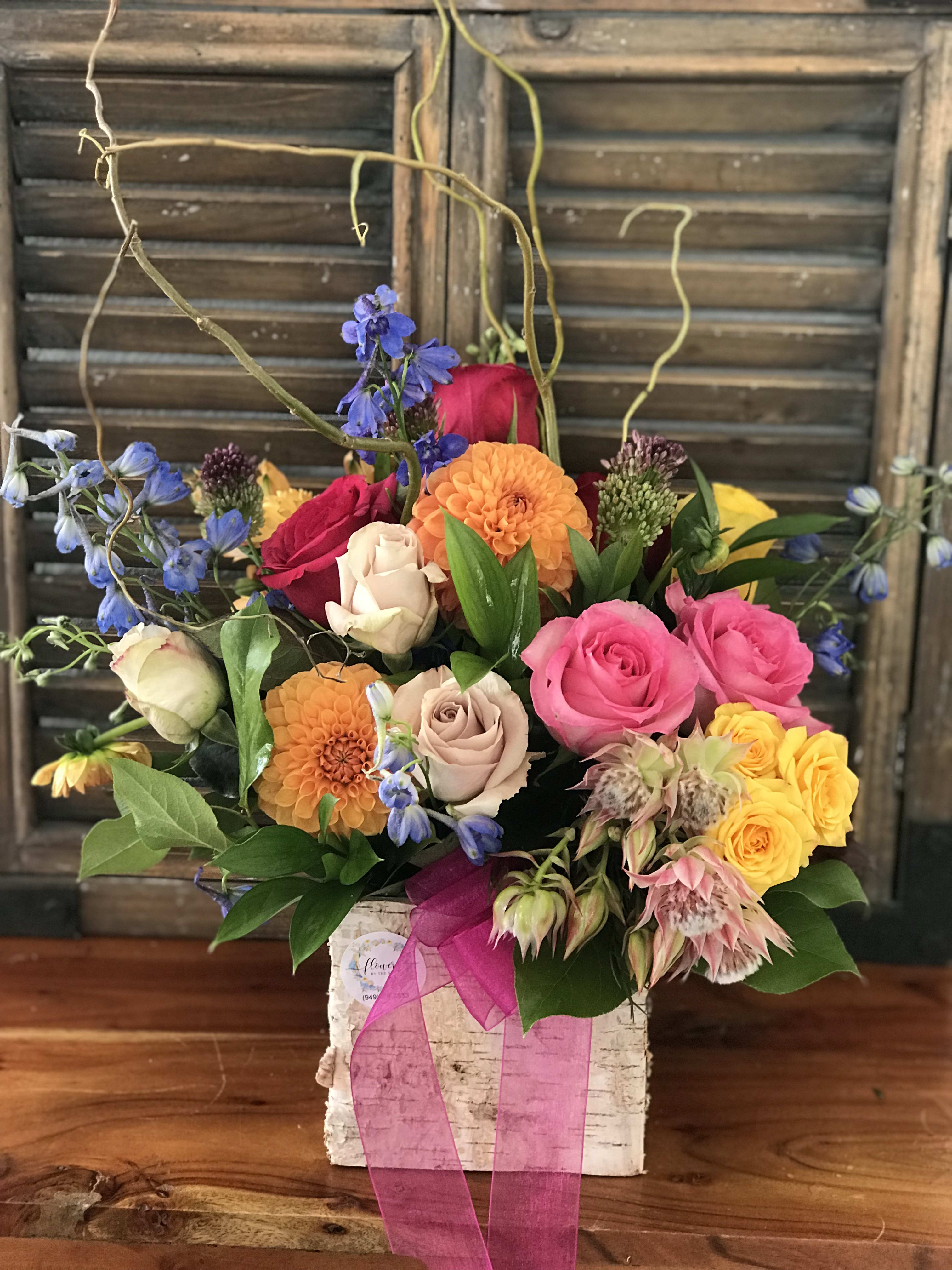 Mixed bouquet of roses, dahlias, and blue flowers in a white box with pink ribbon