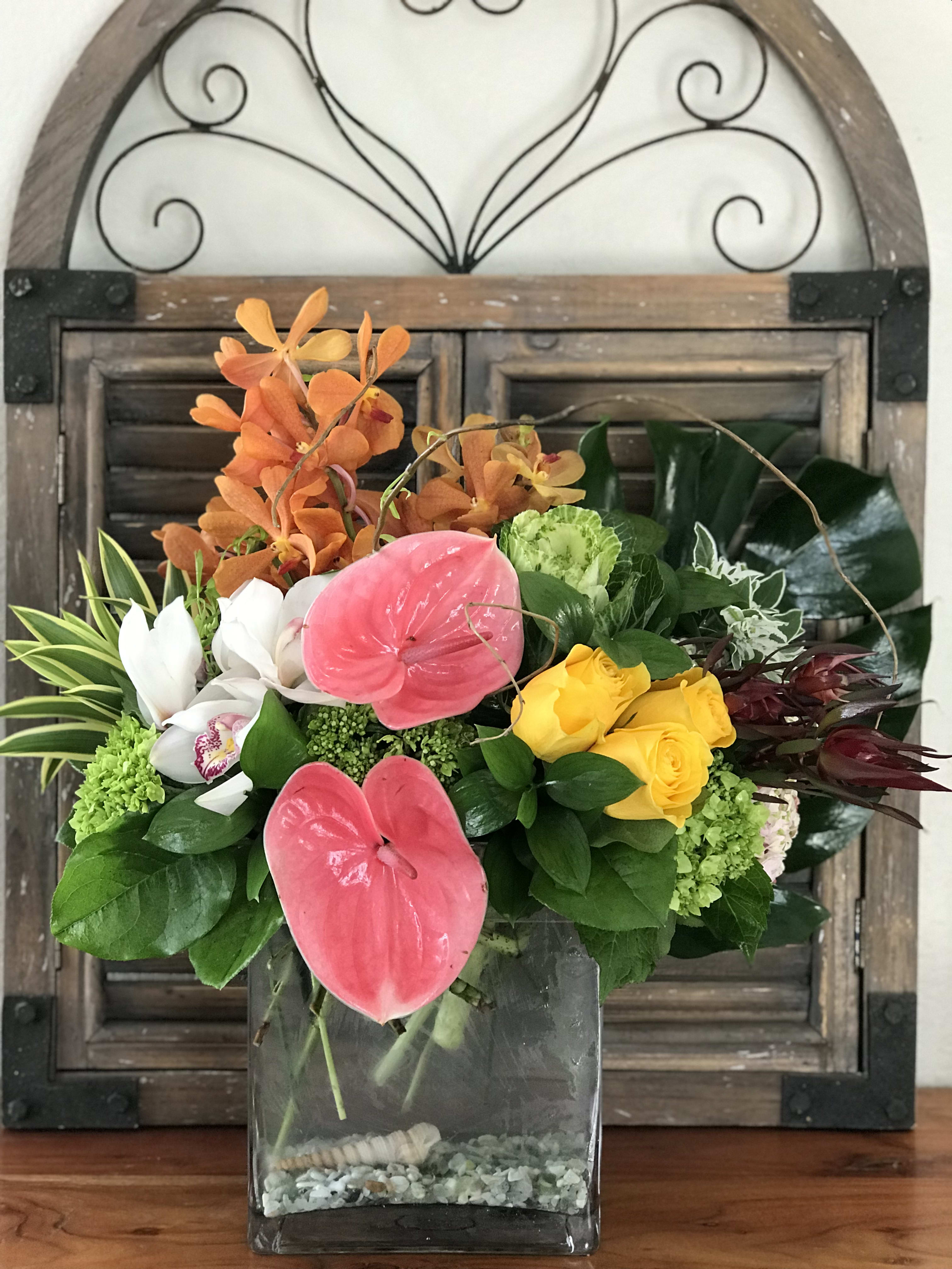 Mixed tropical bouquet in a glass vase with pink anthuriums and yellow roses