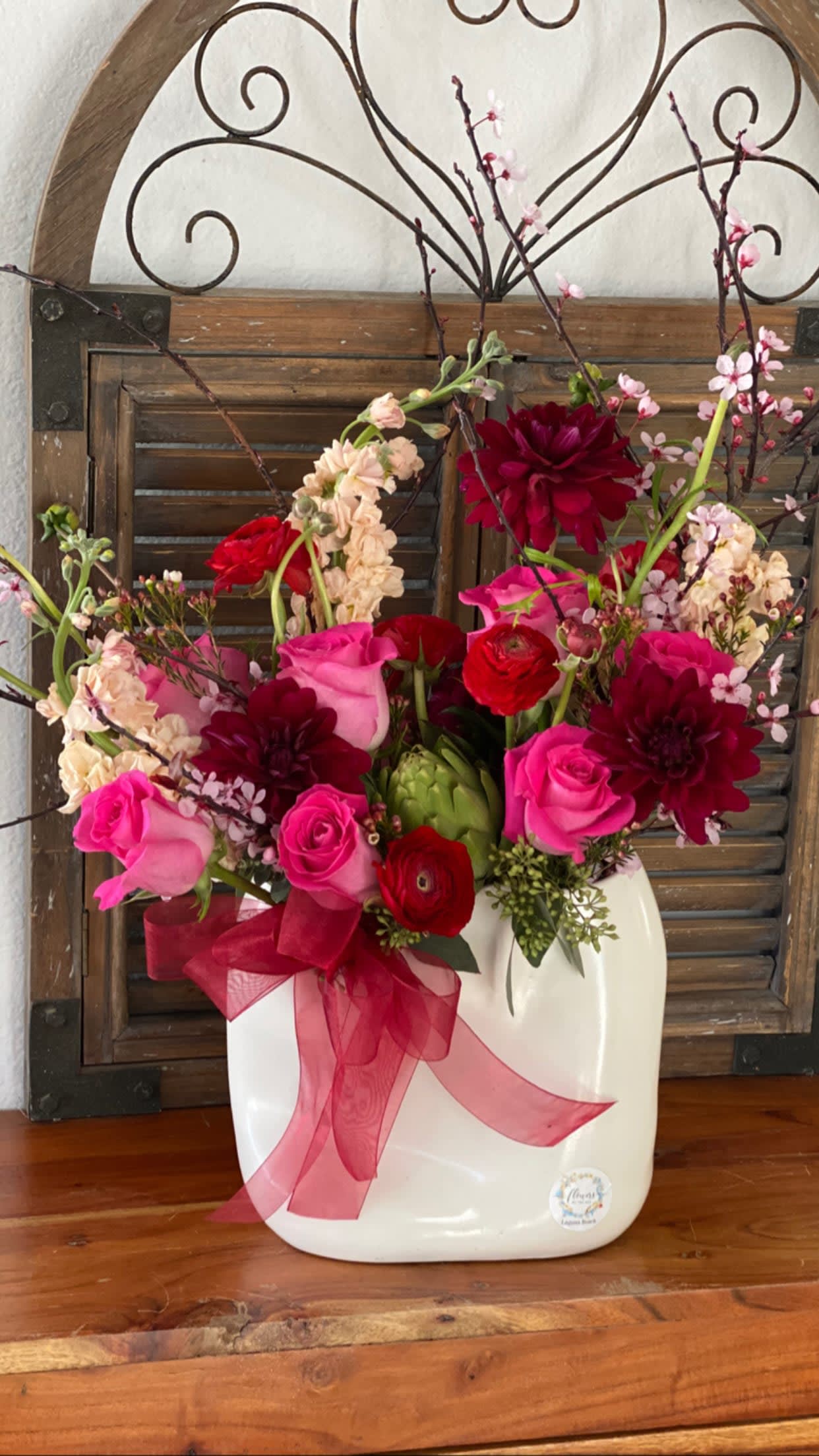 Pink and red floral arrangement in a white vase with a ribbon