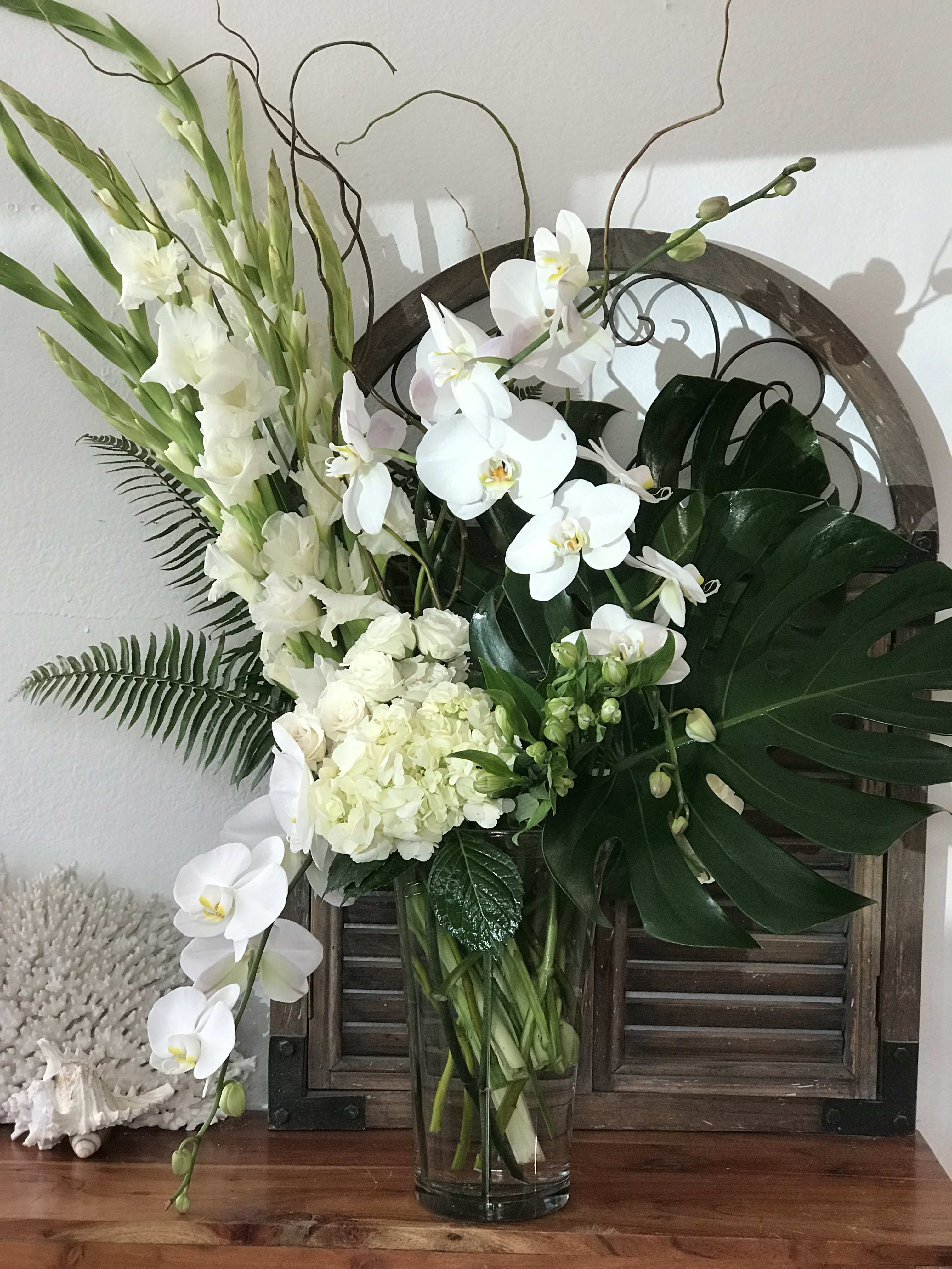 White orchids and gladiolus arranged in a clear glass vase