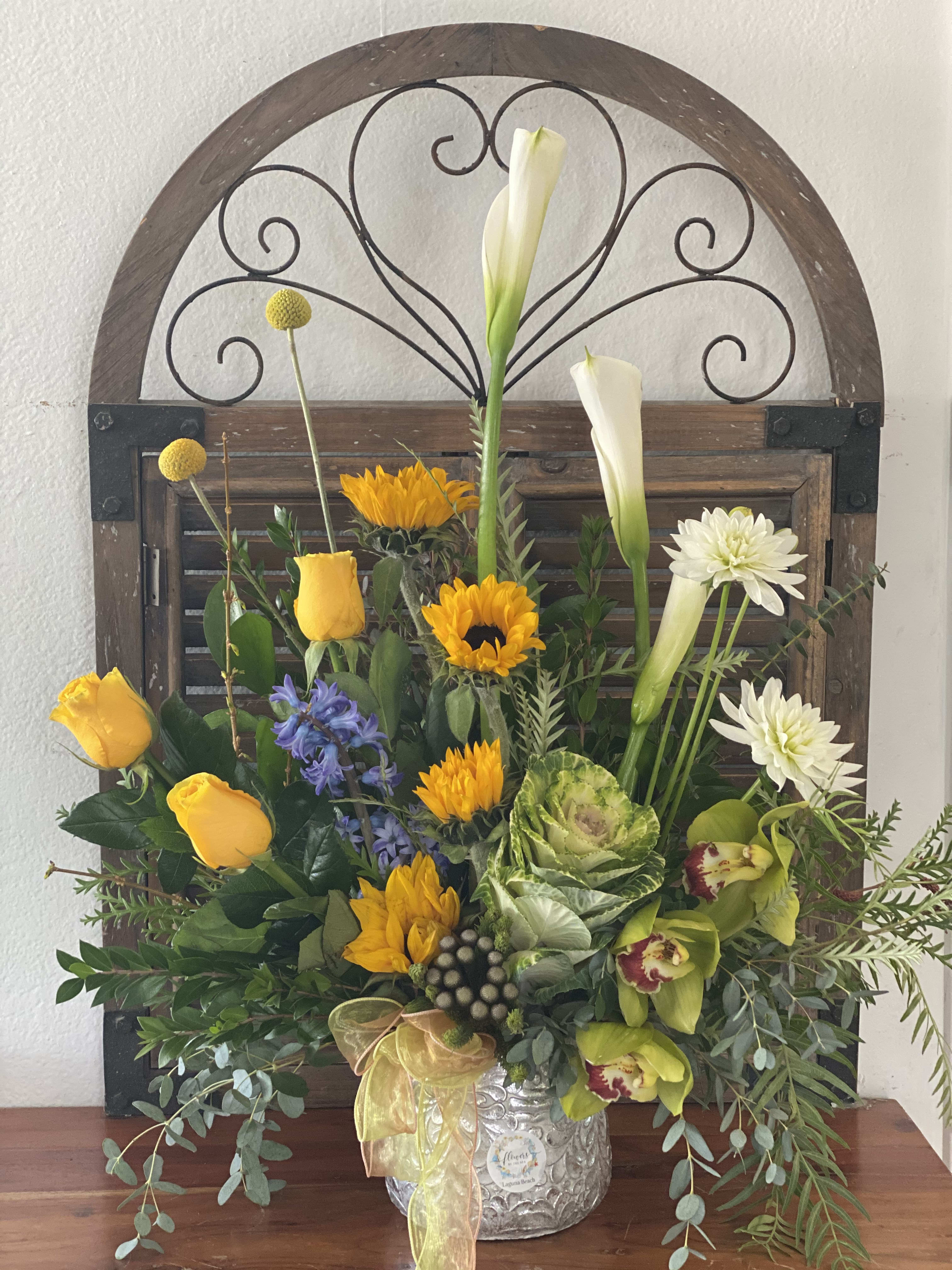 Mixed floral arrangement with yellow roses, white calla lilies, and sunflowers in a silver vase