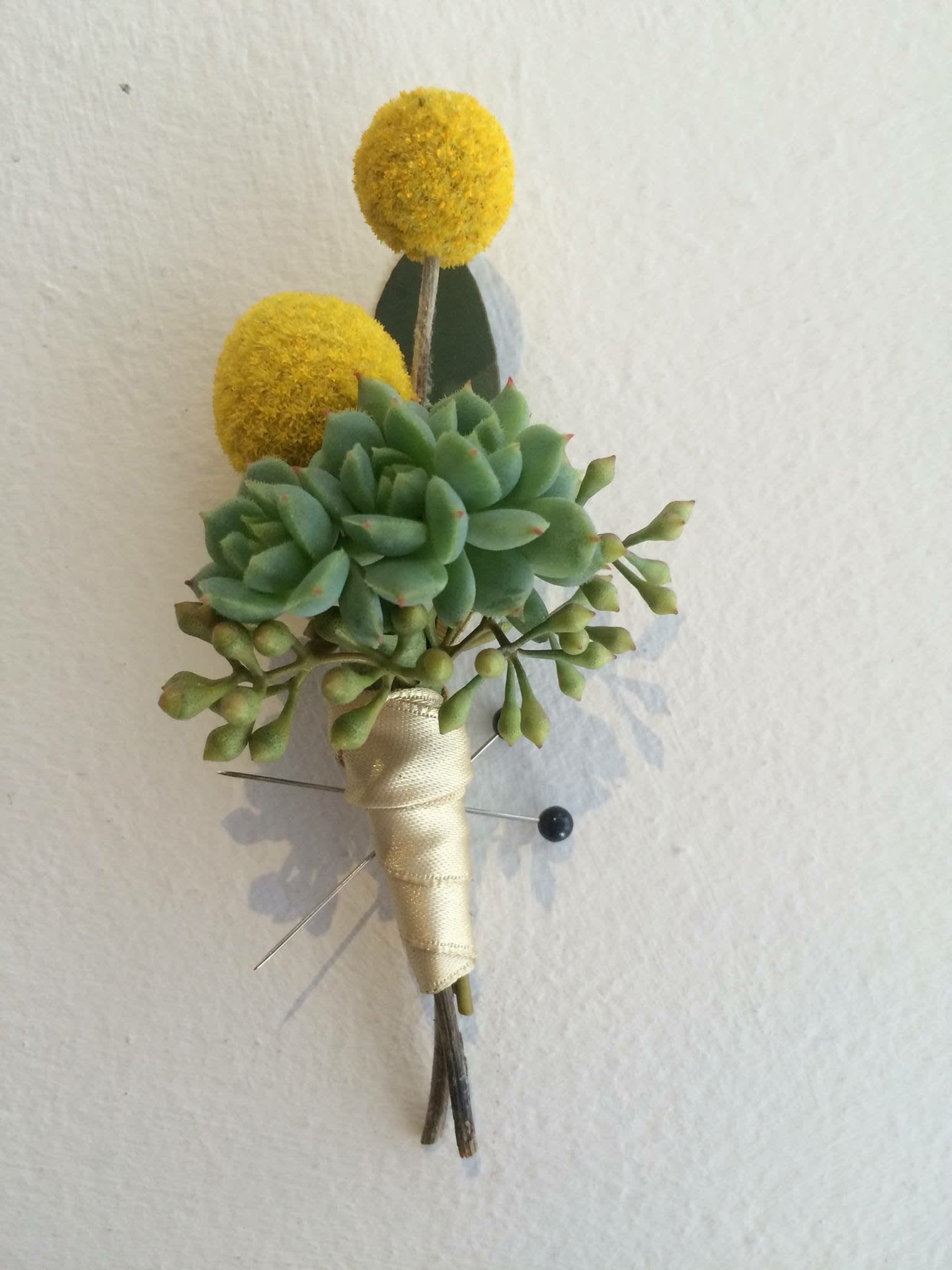 Succulent boutonniere with yellow pom-pom accents and cream ribbon wrap