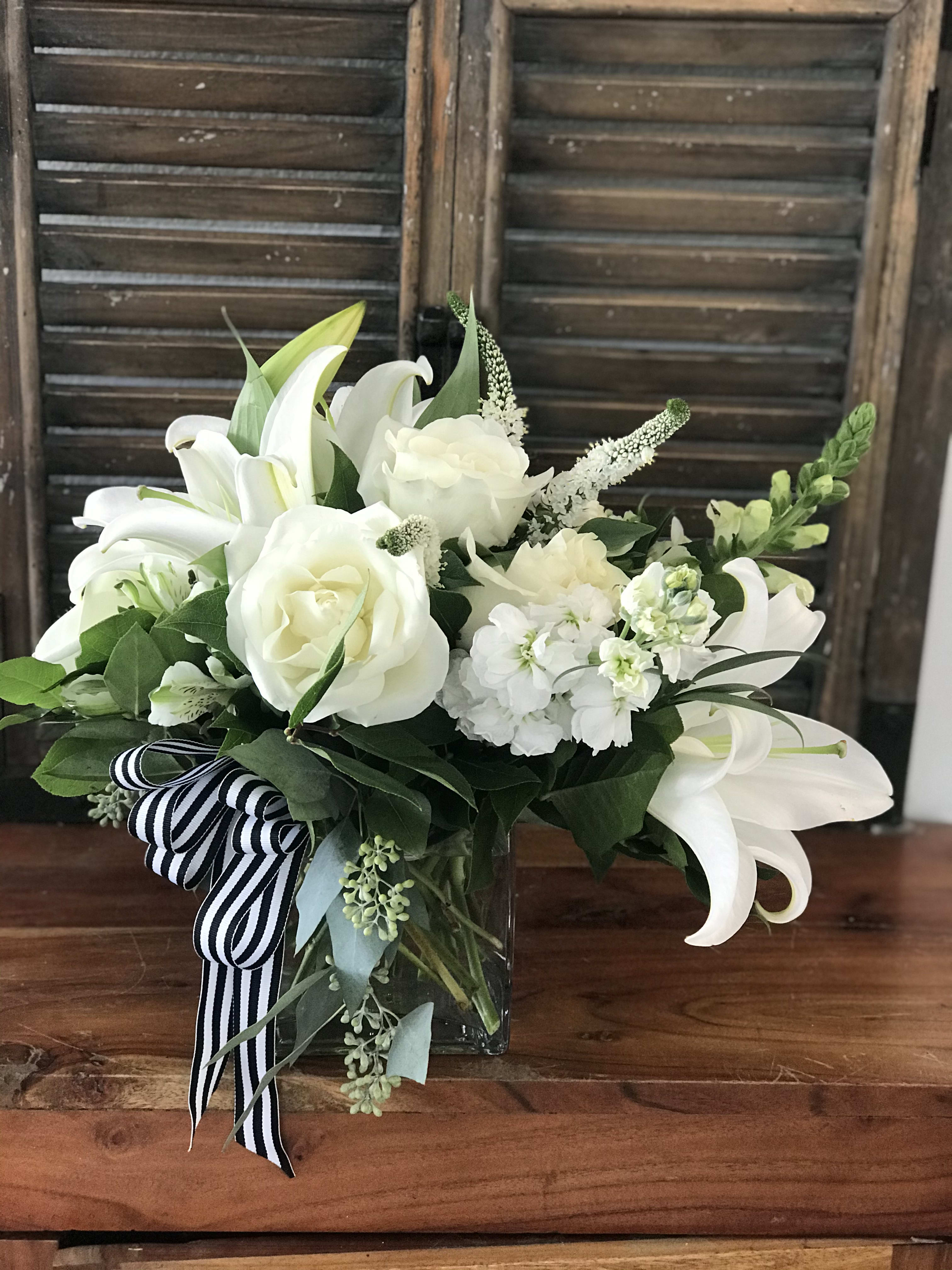 White lilies and roses in a glass vase with a striped ribbon