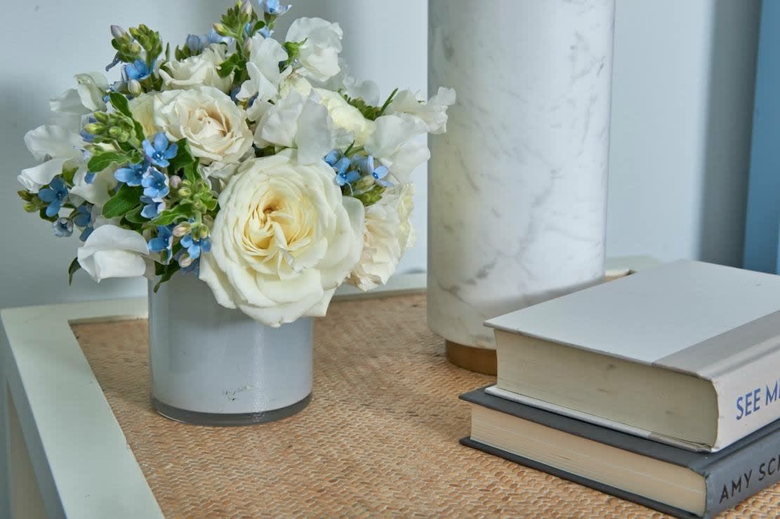 White roses and blue flowers arranged in a small vase on a table