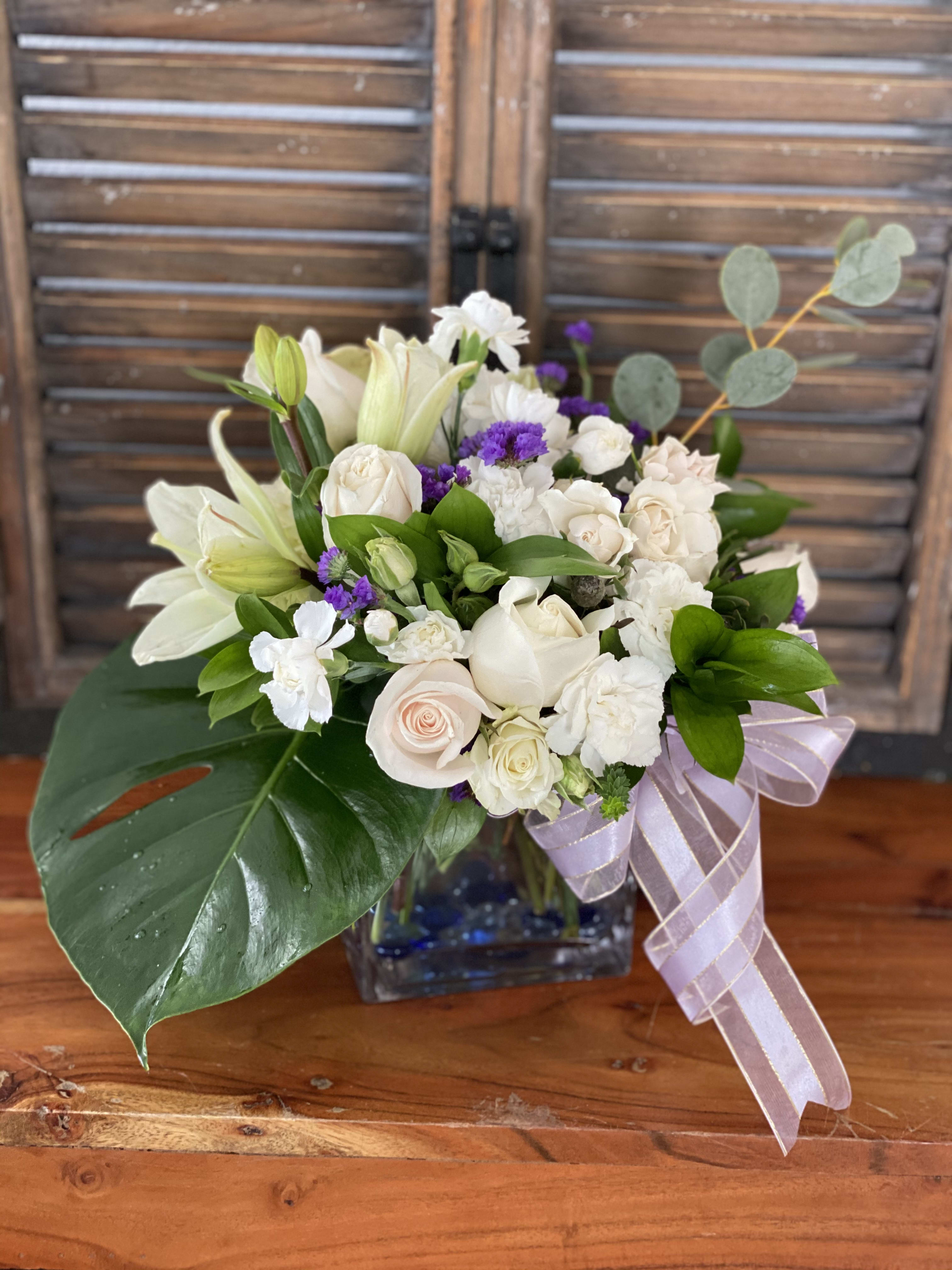 White roses and lilies in a glass vase with a lavender ribbon