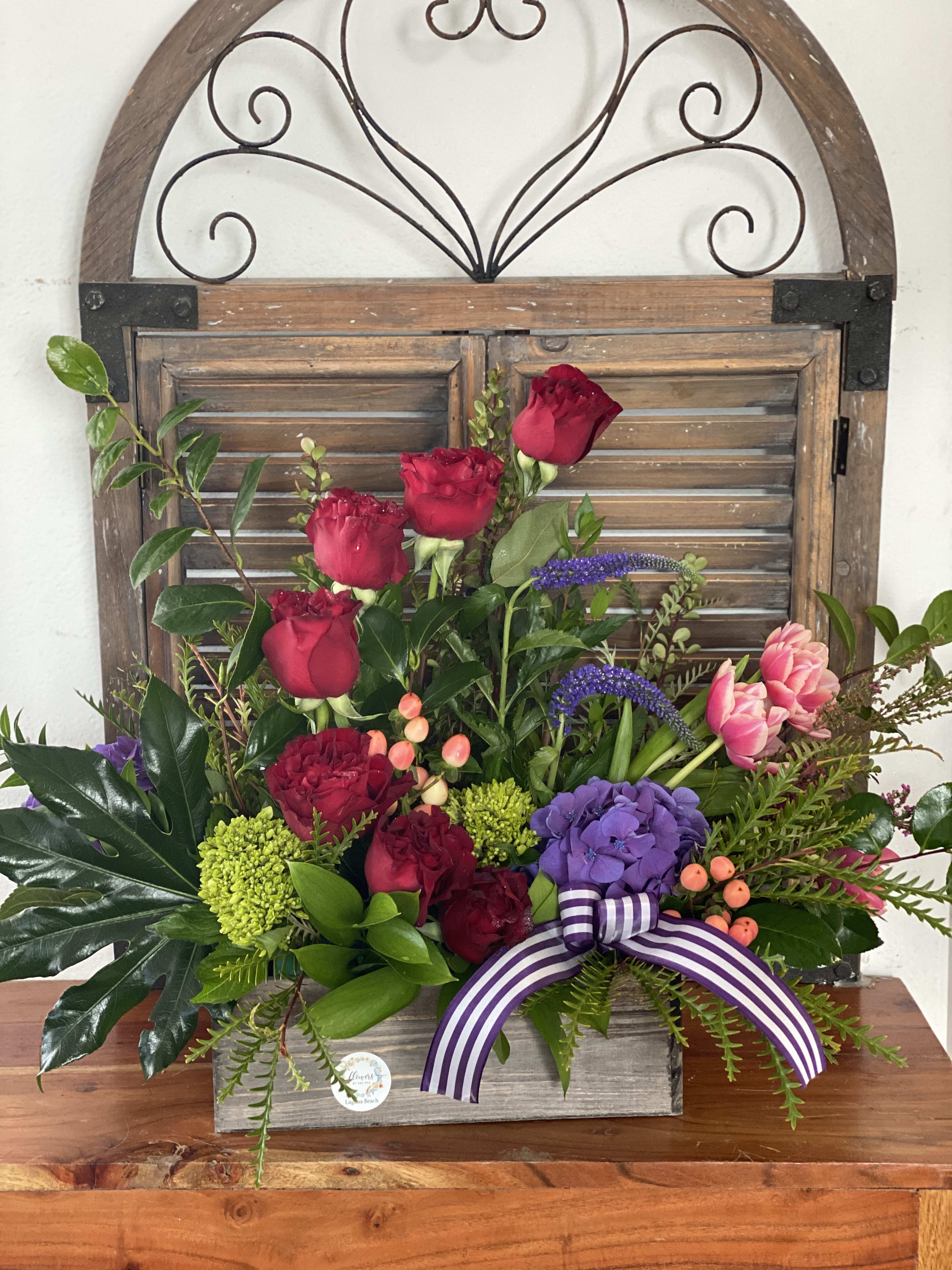 Mixed bouquet with red roses, purple hydrangea, and pink tulips in a wooden box