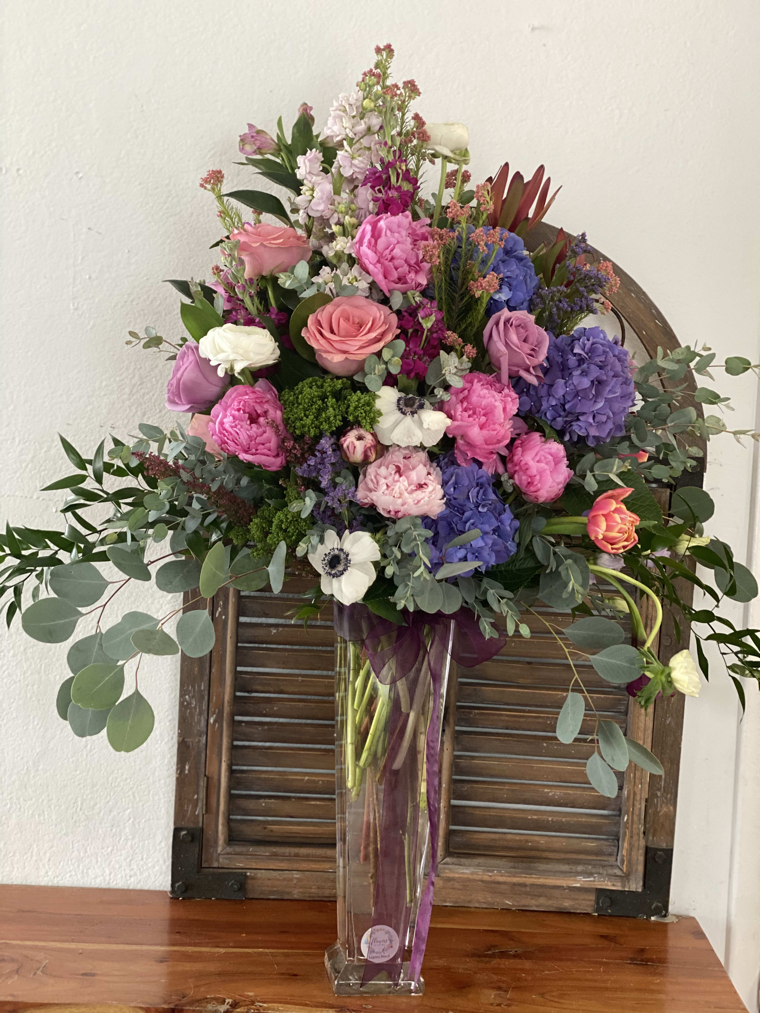 Mixed bouquet of pink, purple, and white flowers in a tall clear vase