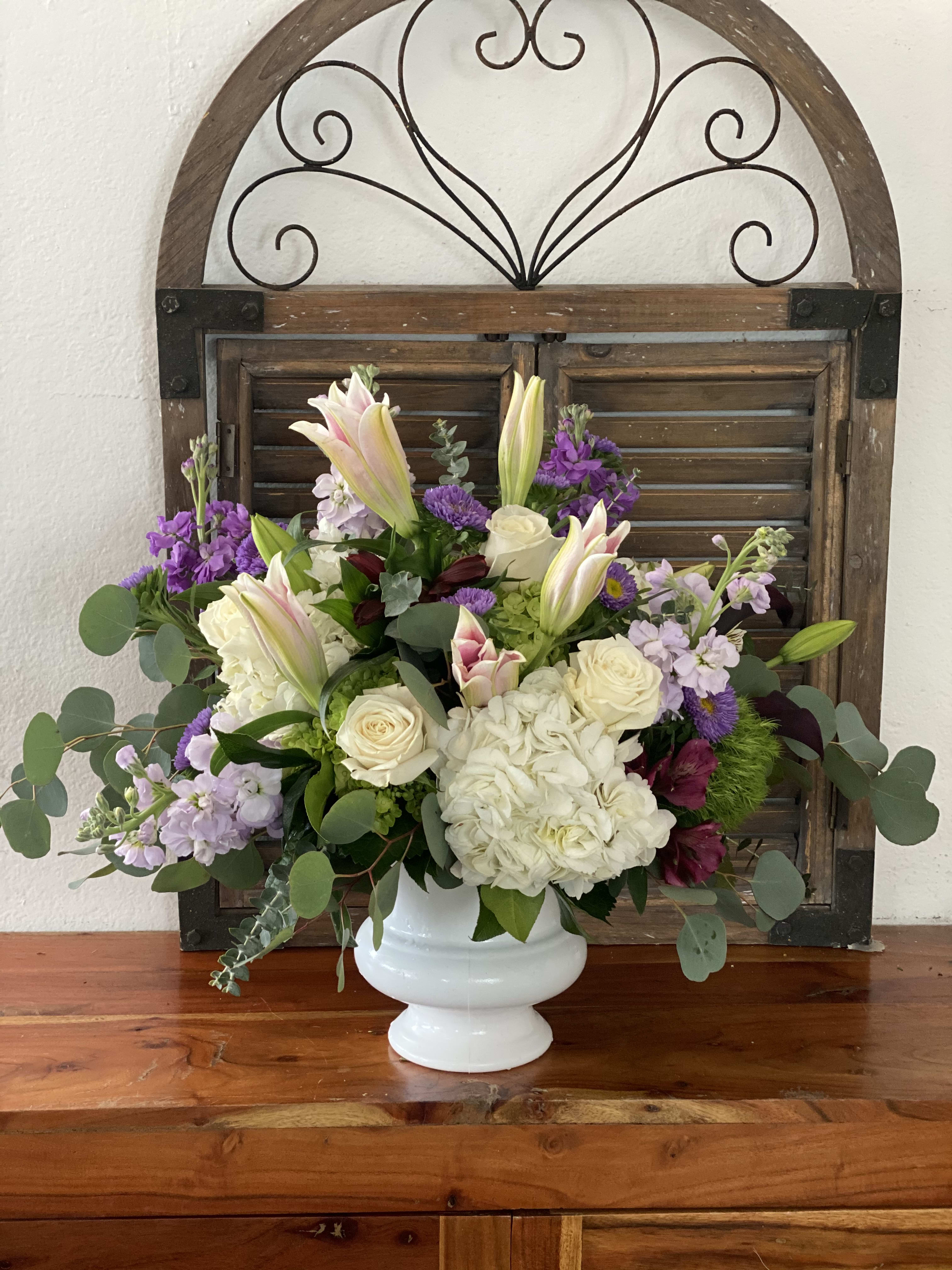 White vase arrangement with lilies, roses, hydrangea, and purple flowers