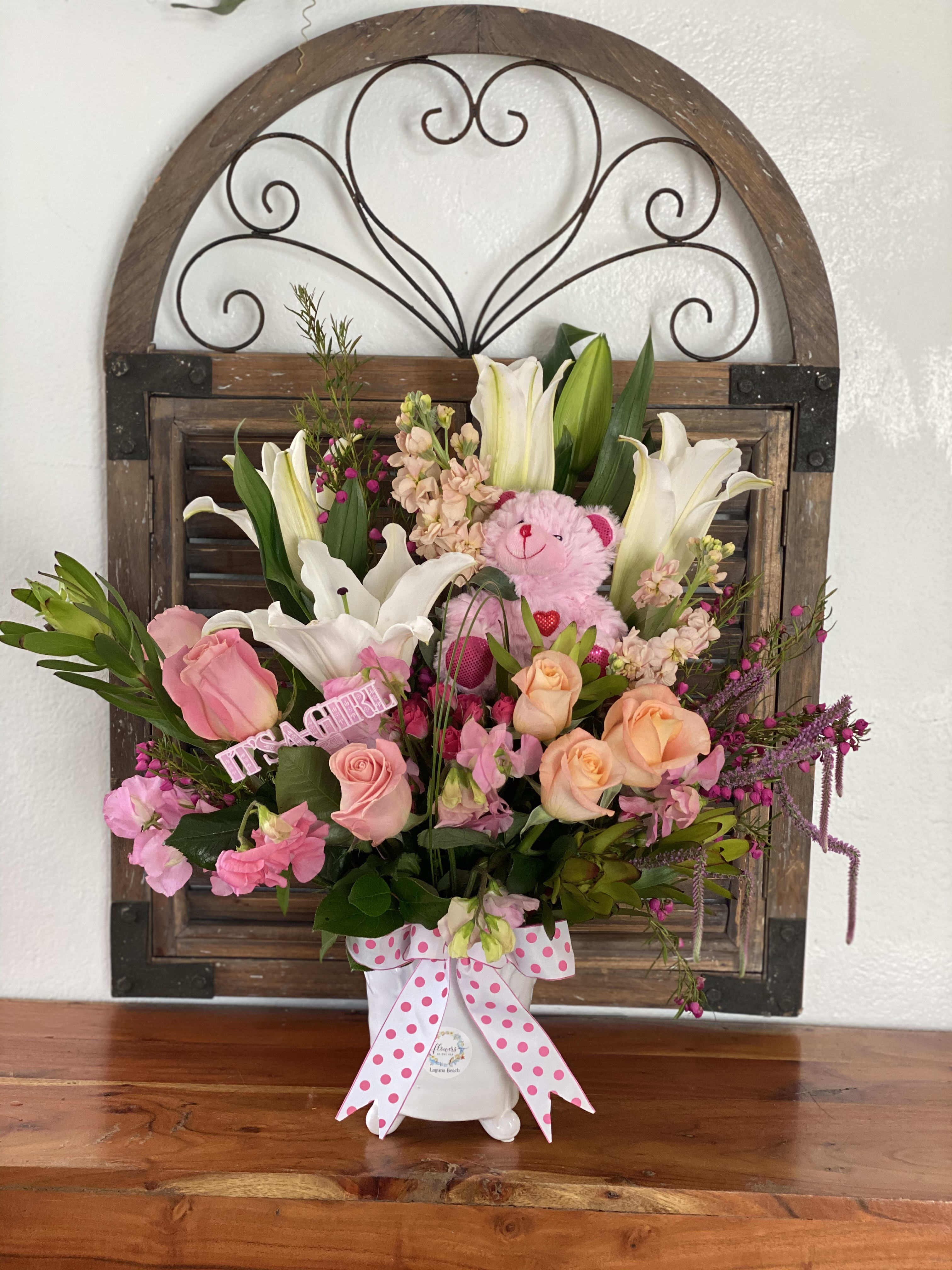 Pink and white floral arrangement with a teddy bear in a white vase