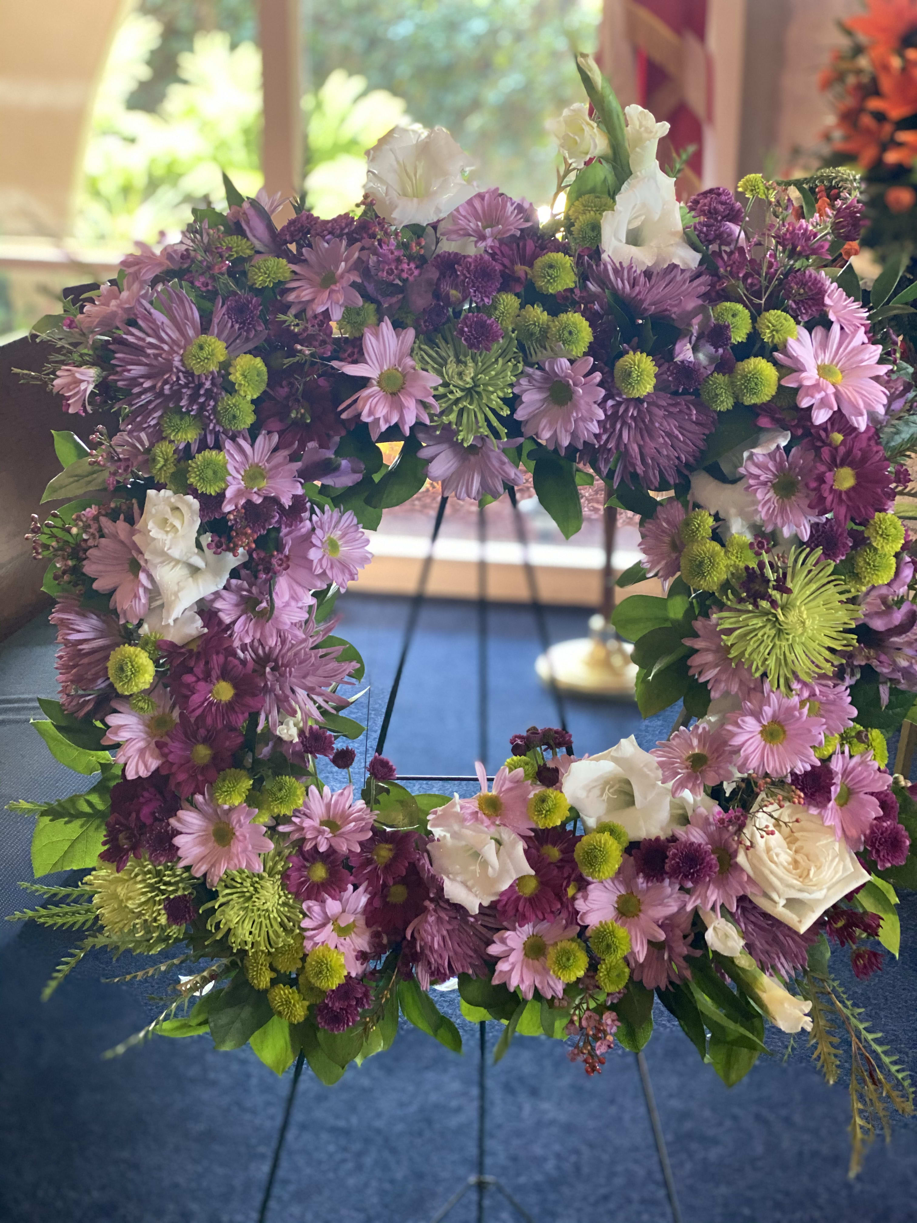Purple and pink floral wreath with white roses on a stand
