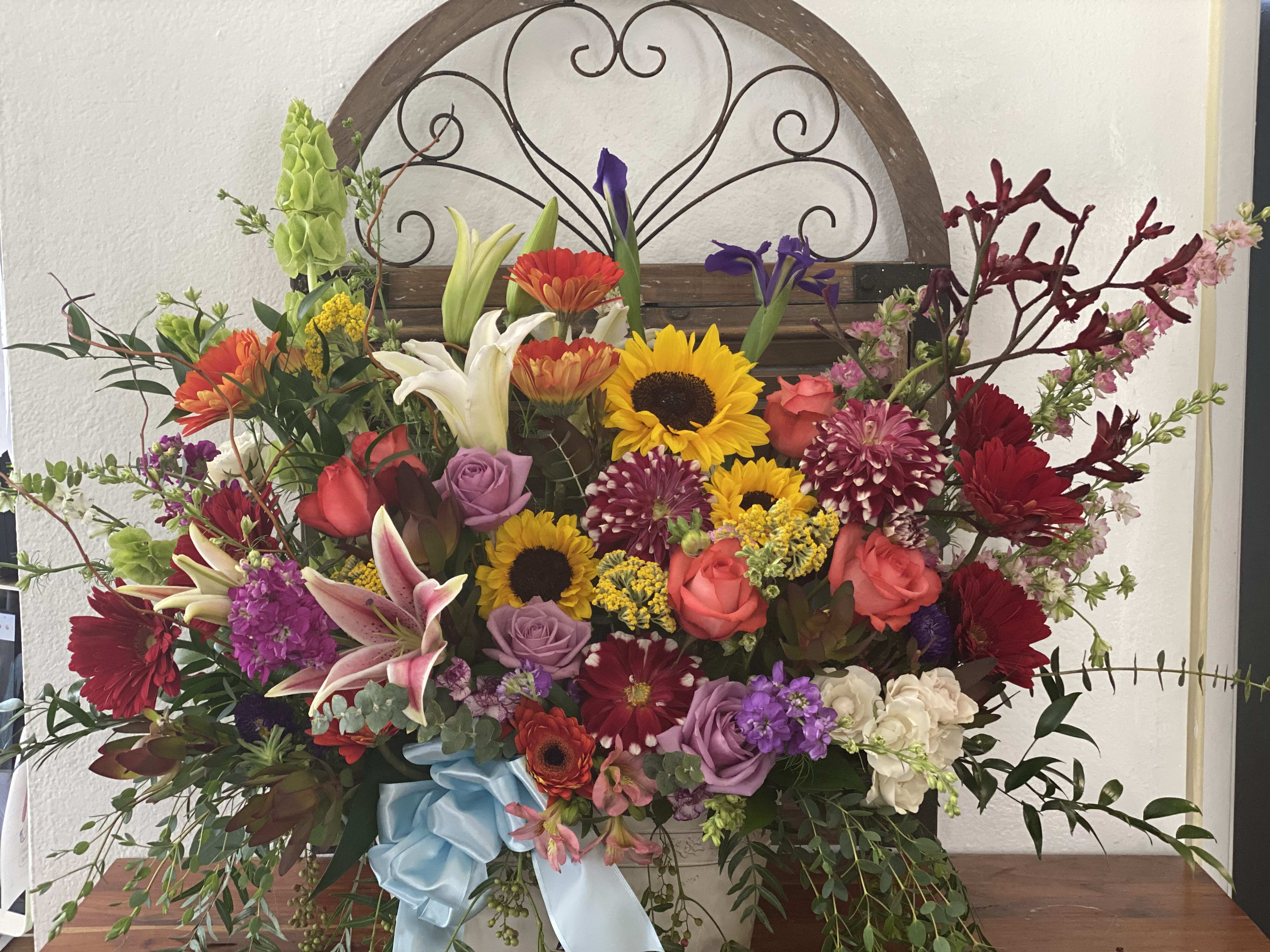 Large mixed flower arrangement with sunflowers, roses, lilies, and a blue ribbon