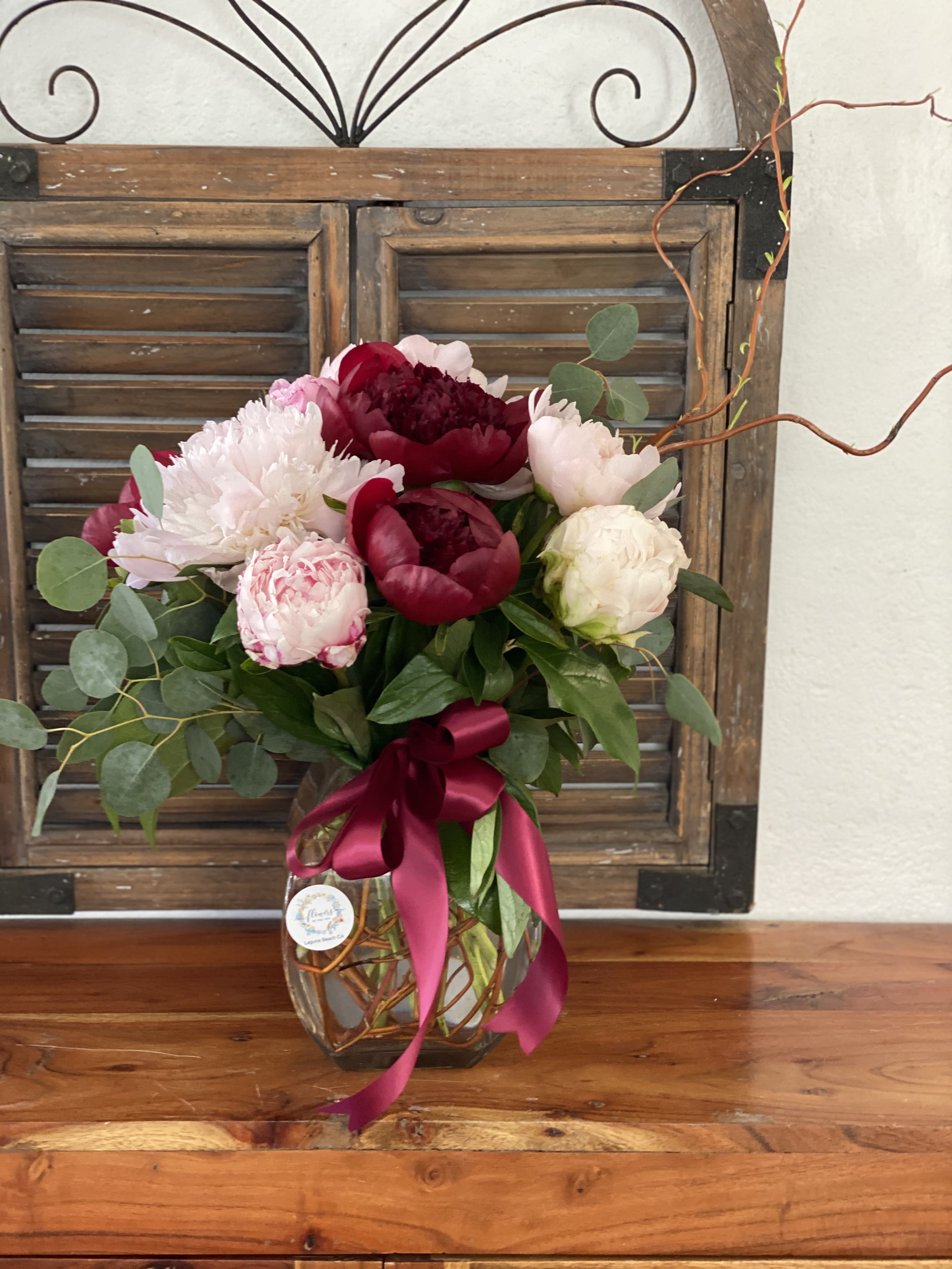 Bouquet of pink and burgundy peonies in a glass vase with a ribbon