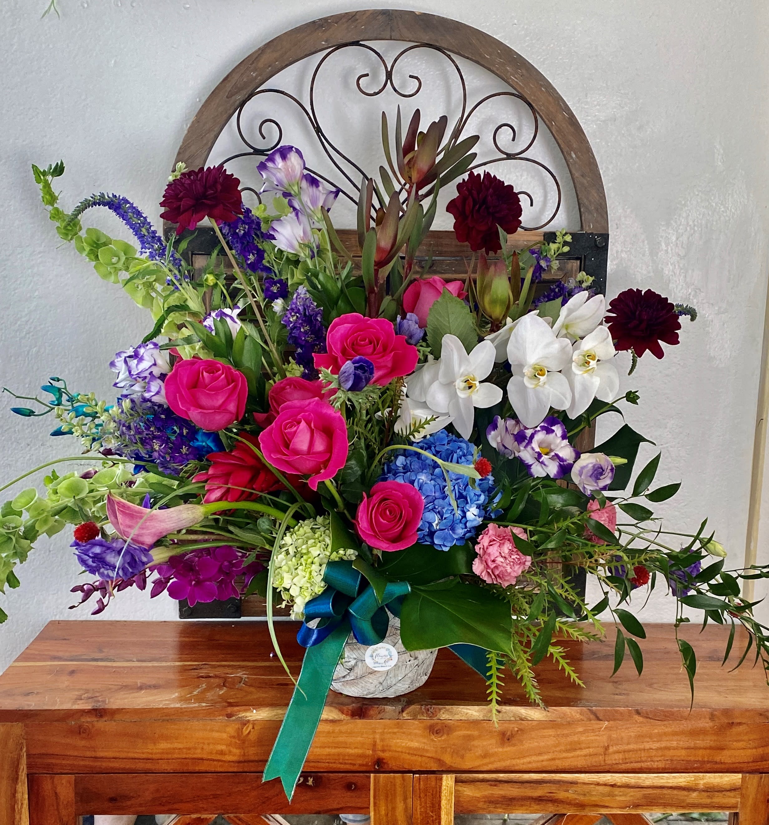 Colorful mixed flower arrangement in a white container with a teal ribbon