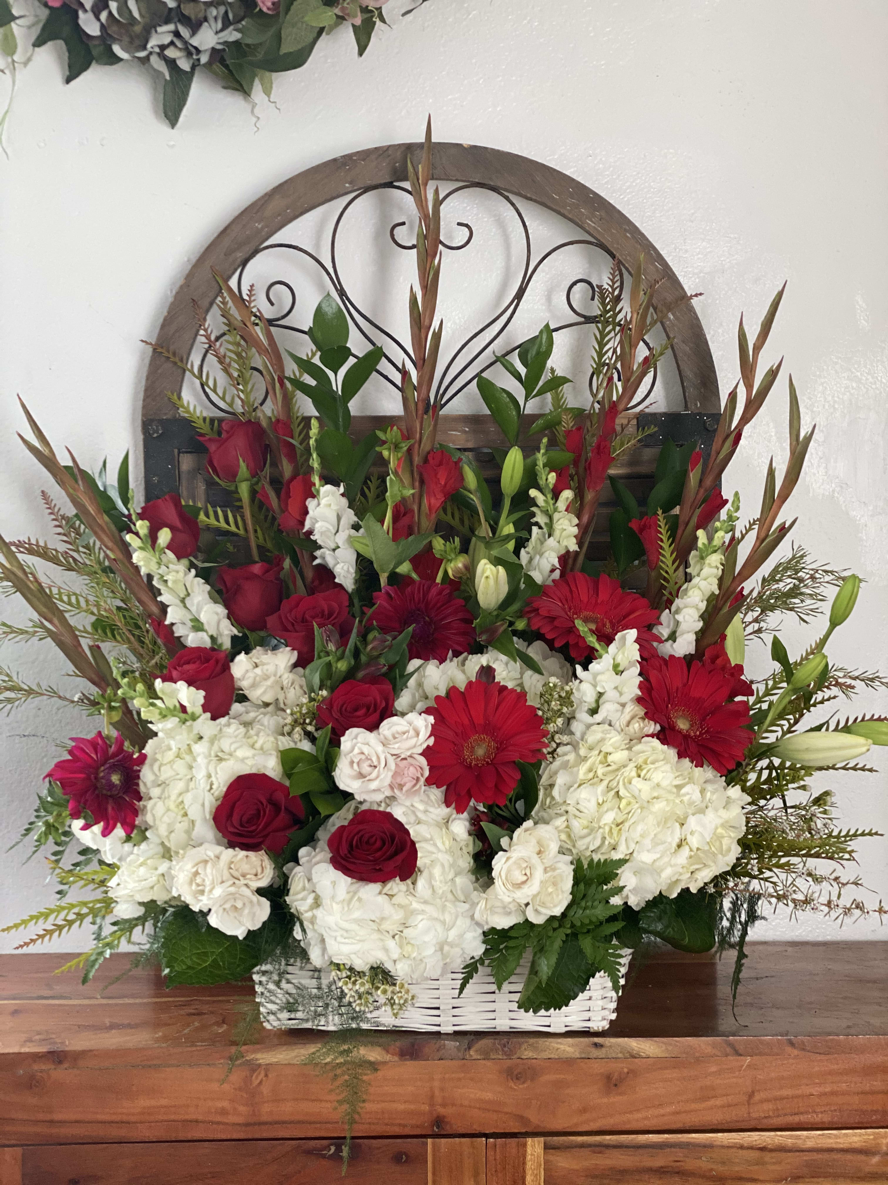 Basket arrangement of red roses, white hydrangeas, and red gerbera daisies