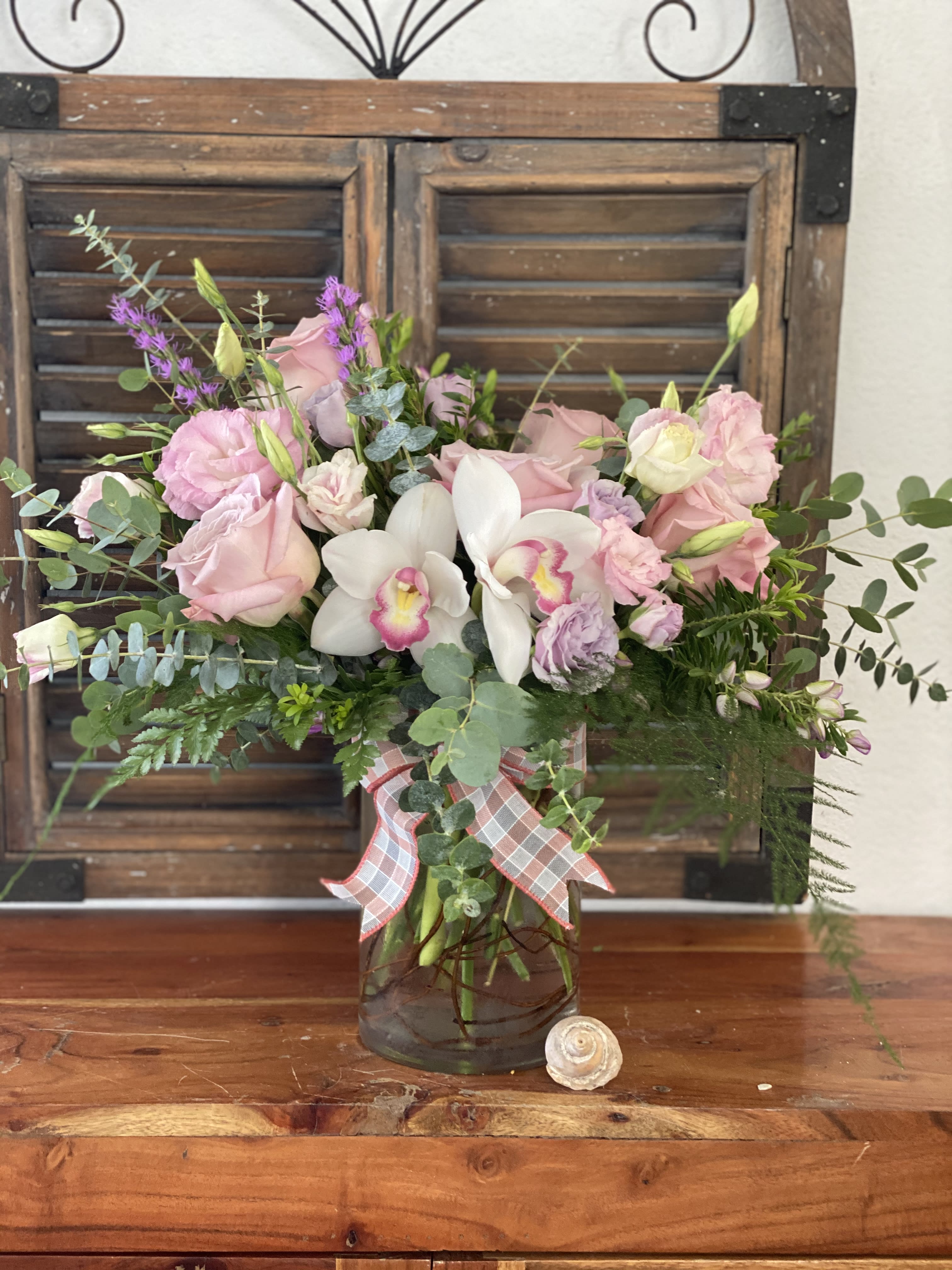 Pink and white floral arrangement in a glass vase with a plaid ribbon