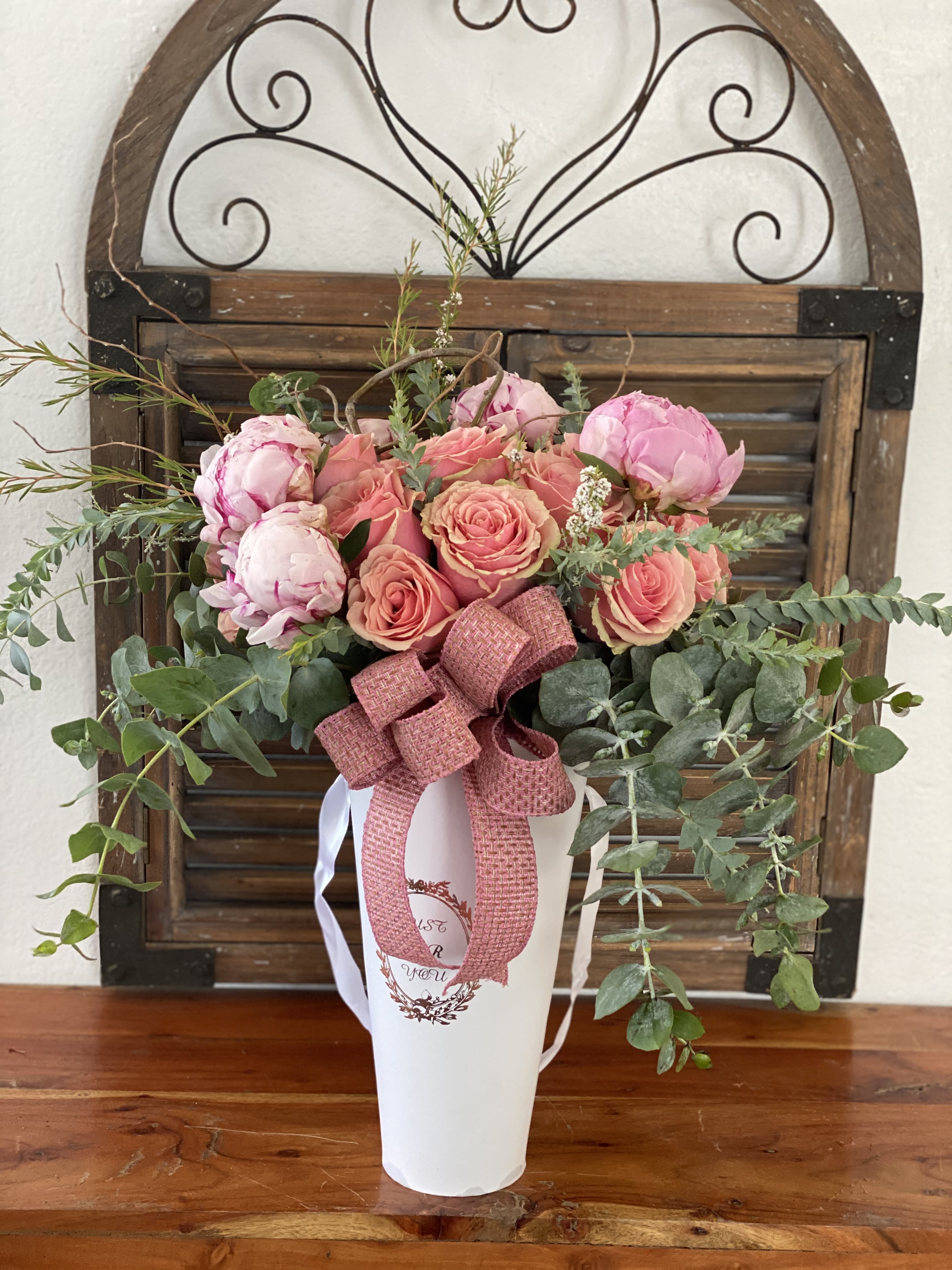 Pink roses and peonies arranged in a white vase with a ribbon
