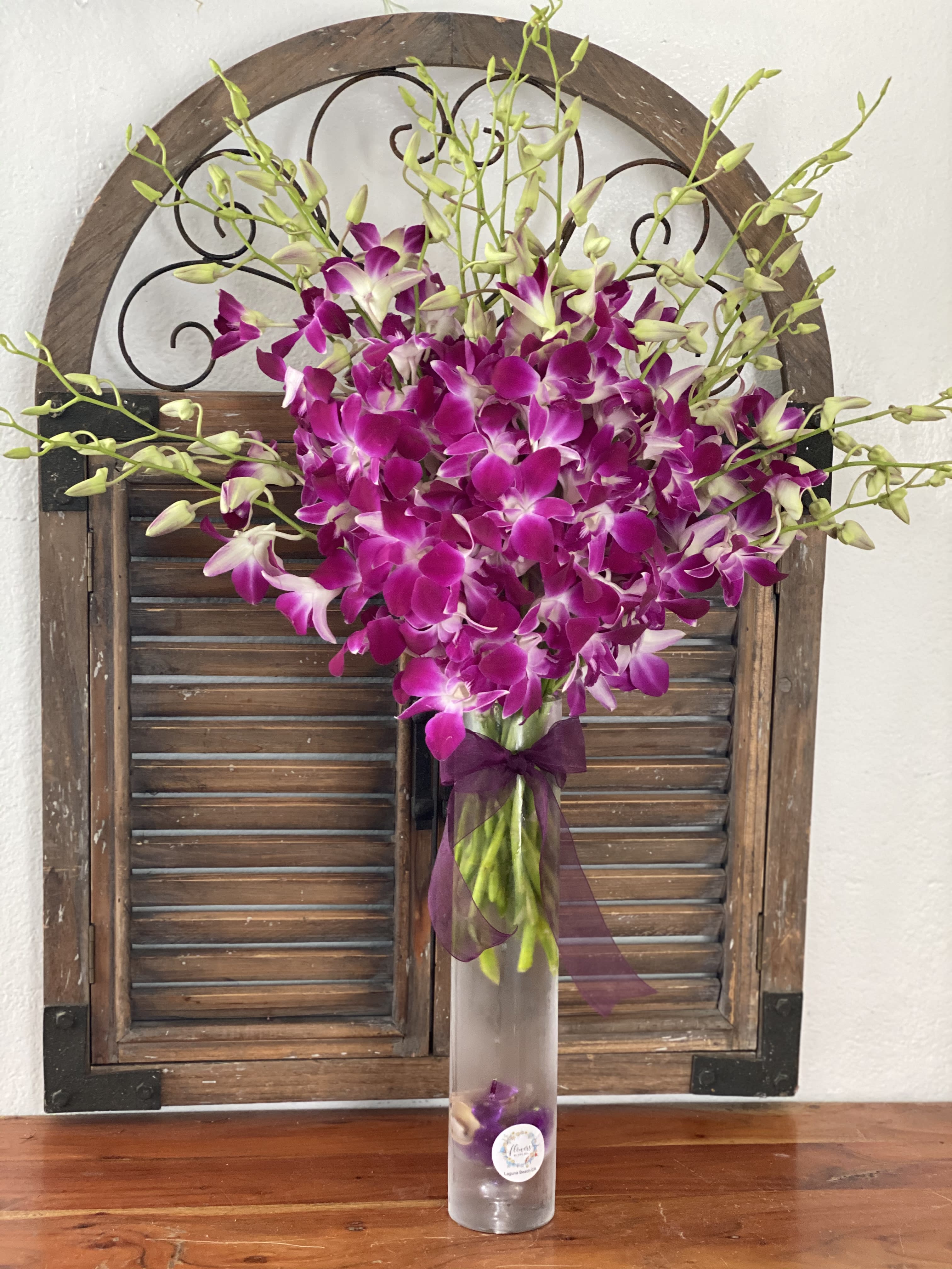 Purple orchids arranged in a tall glass vase with a ribbon.