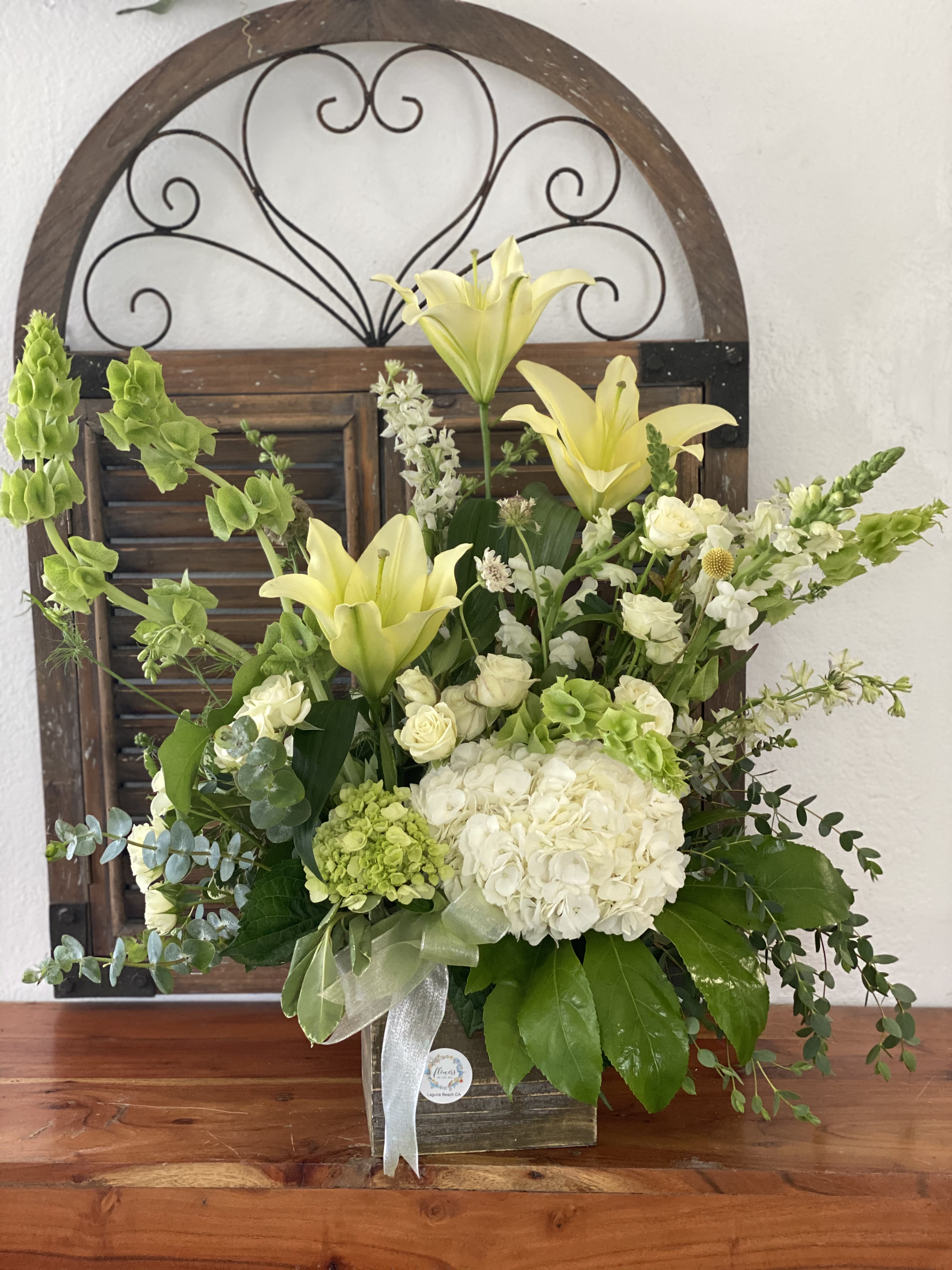 White and green floral arrangement with lilies and roses in a wooden container
