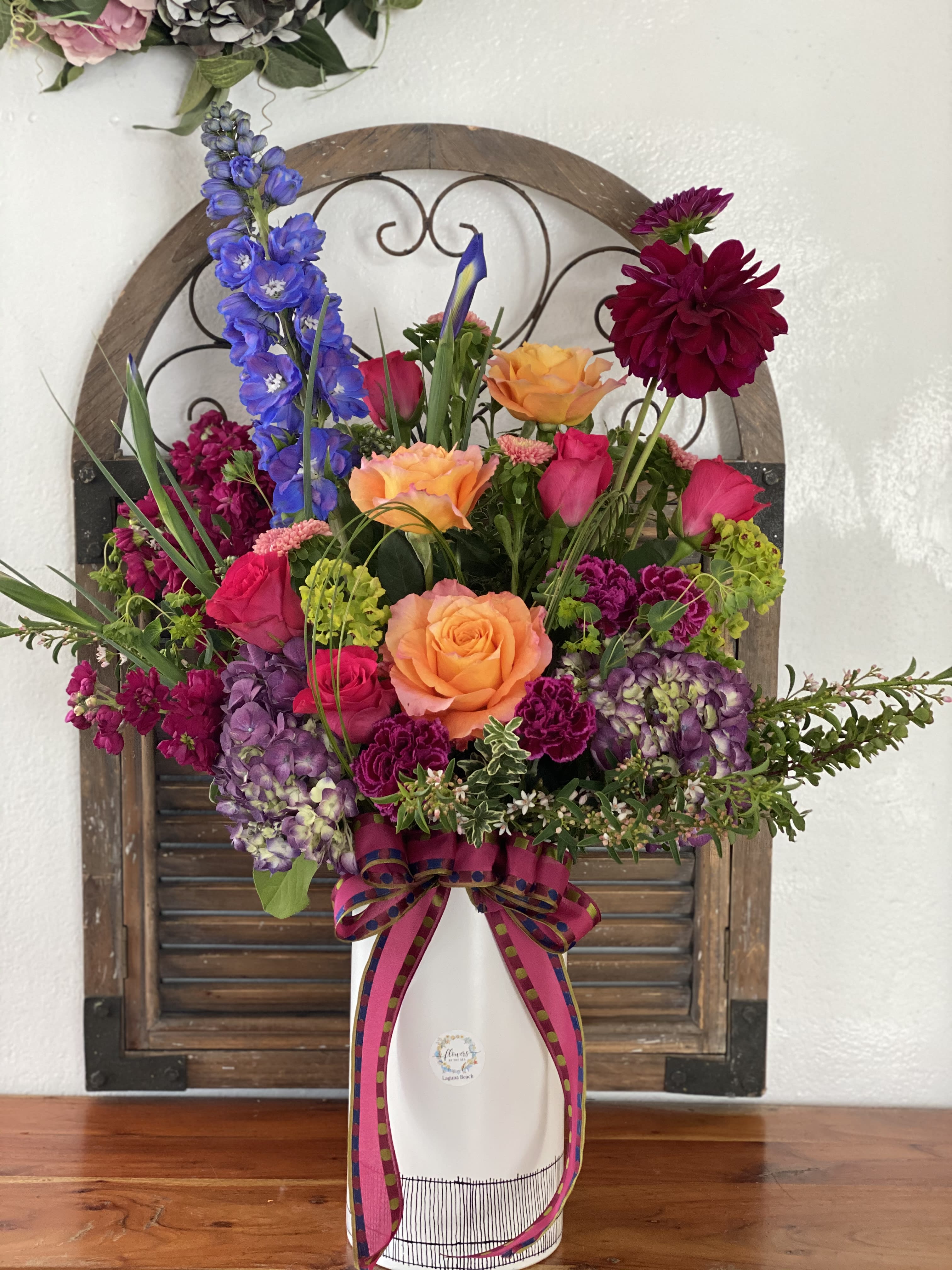 Colorful mixed flower arrangement in a white vase with a ribbon bow