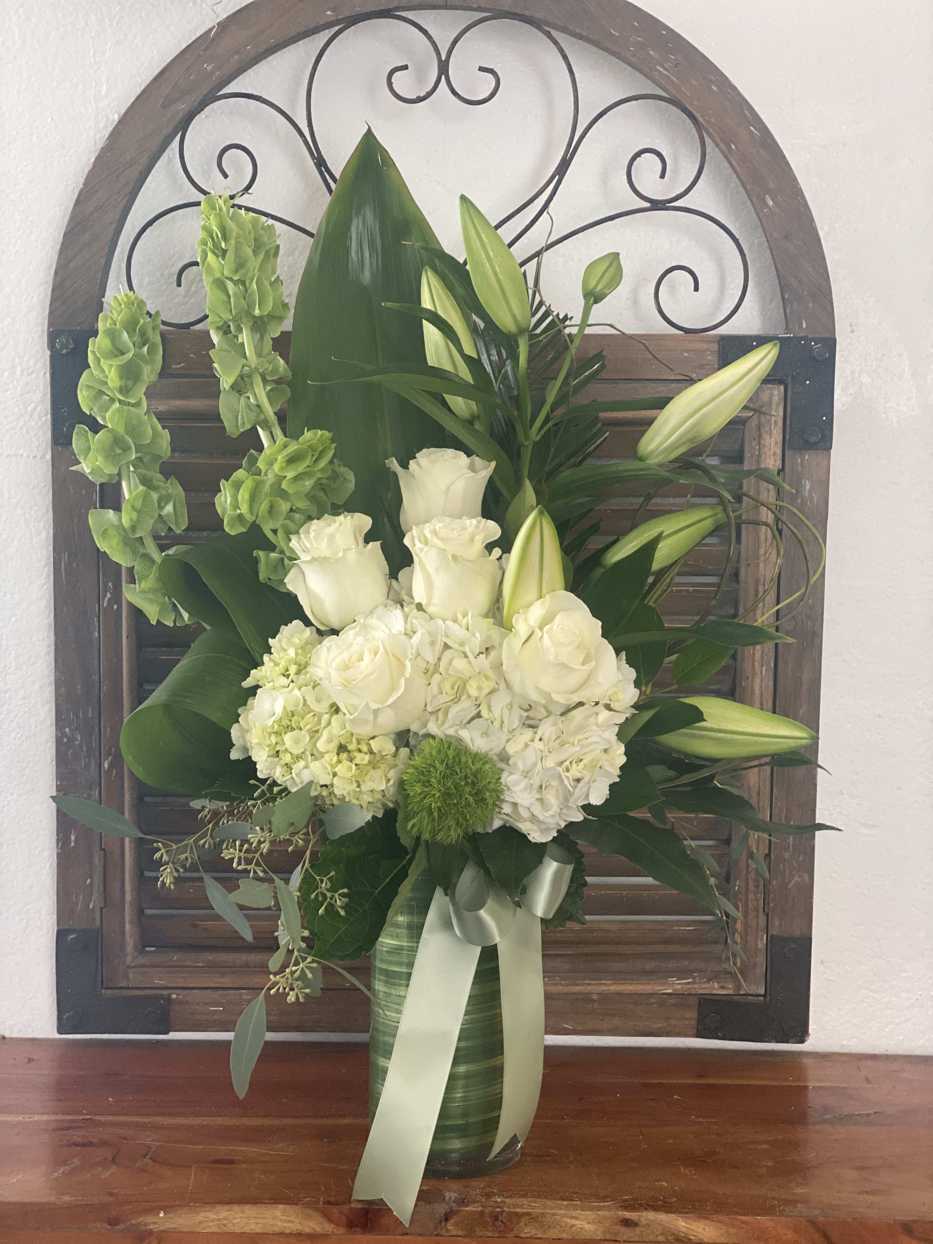 White roses and lilies arranged in a green vase with a ribbon