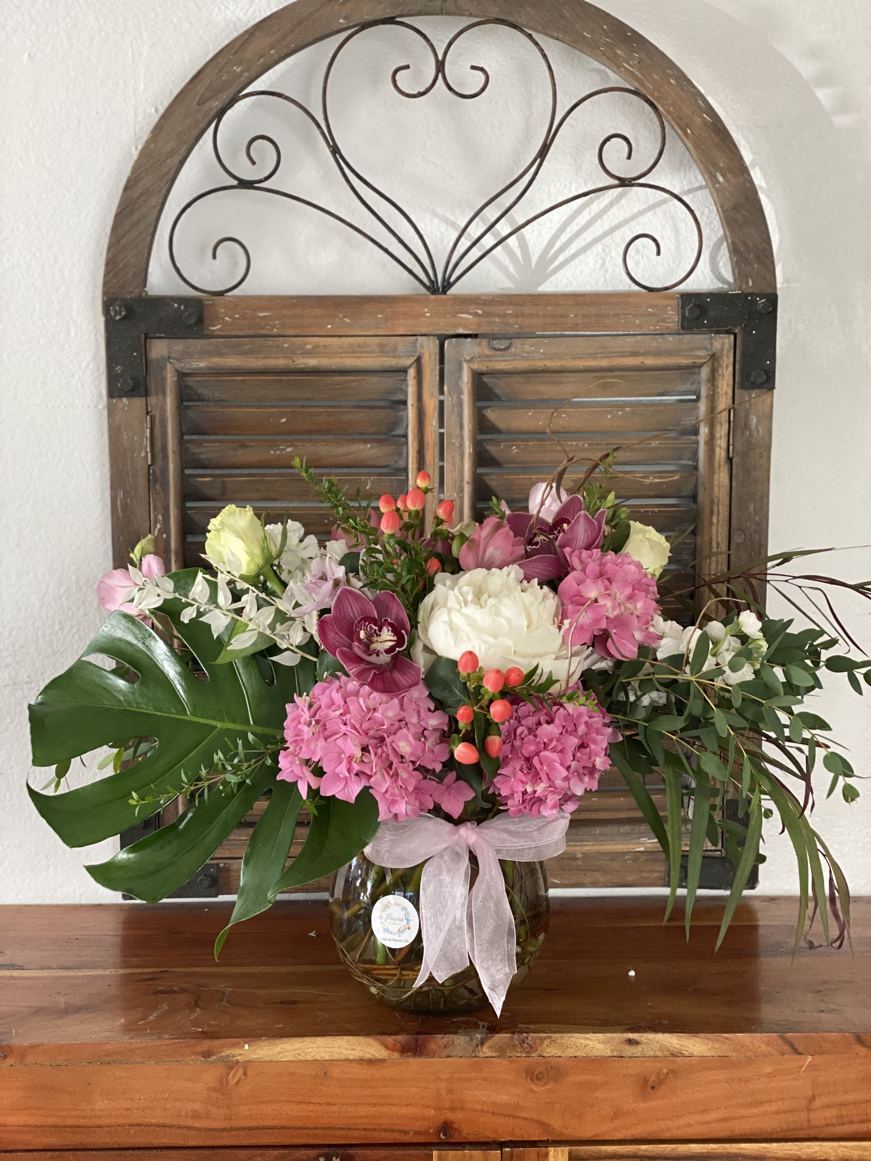 Pink and white floral arrangement in a glass vase with a ribbon