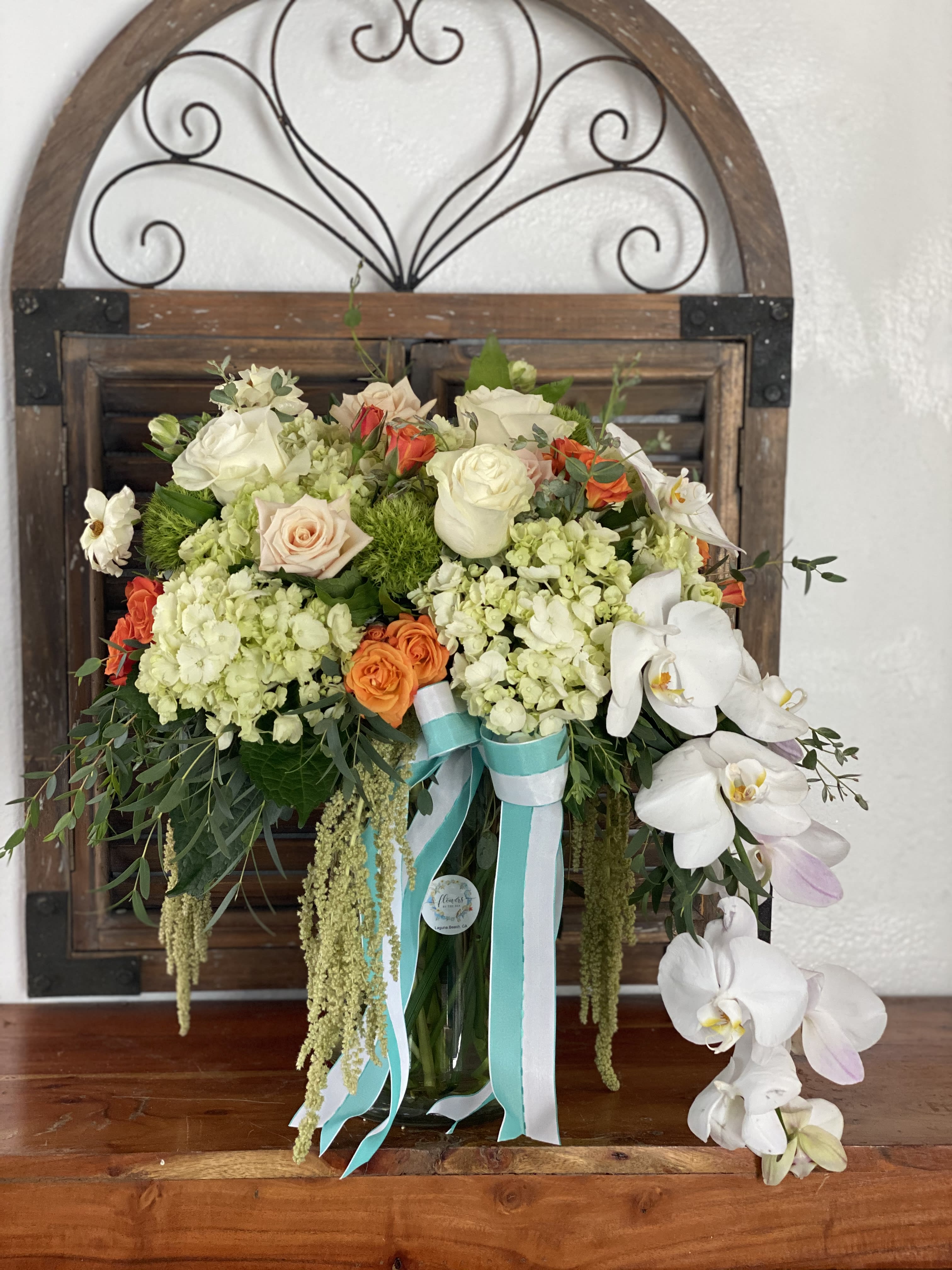 Bouquet of white orchids, roses, and hydrangeas in a glass vase with ribbons