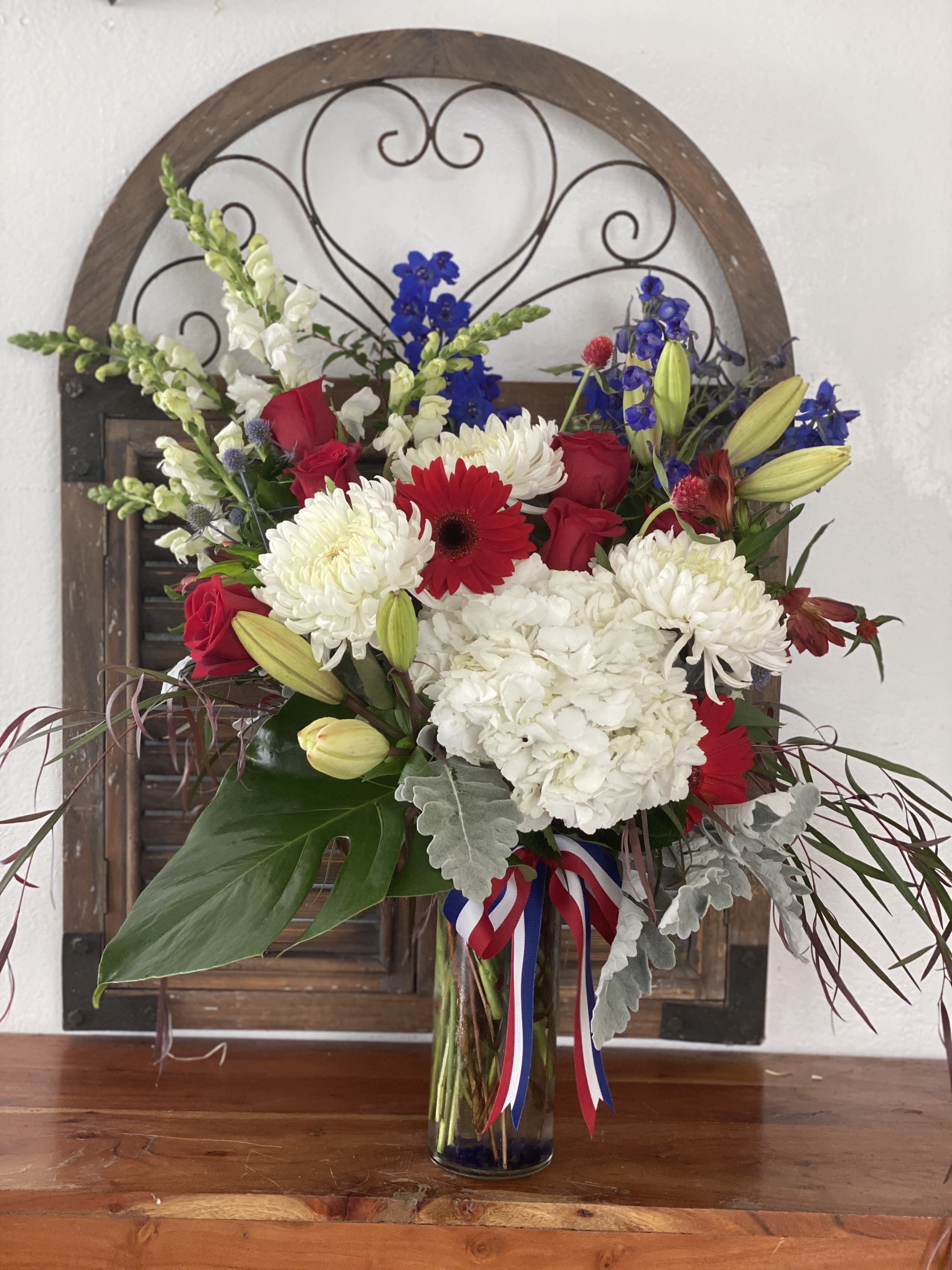 Mixed bouquet of red roses, white chrysanthemums, and blue flowers in a glass vase