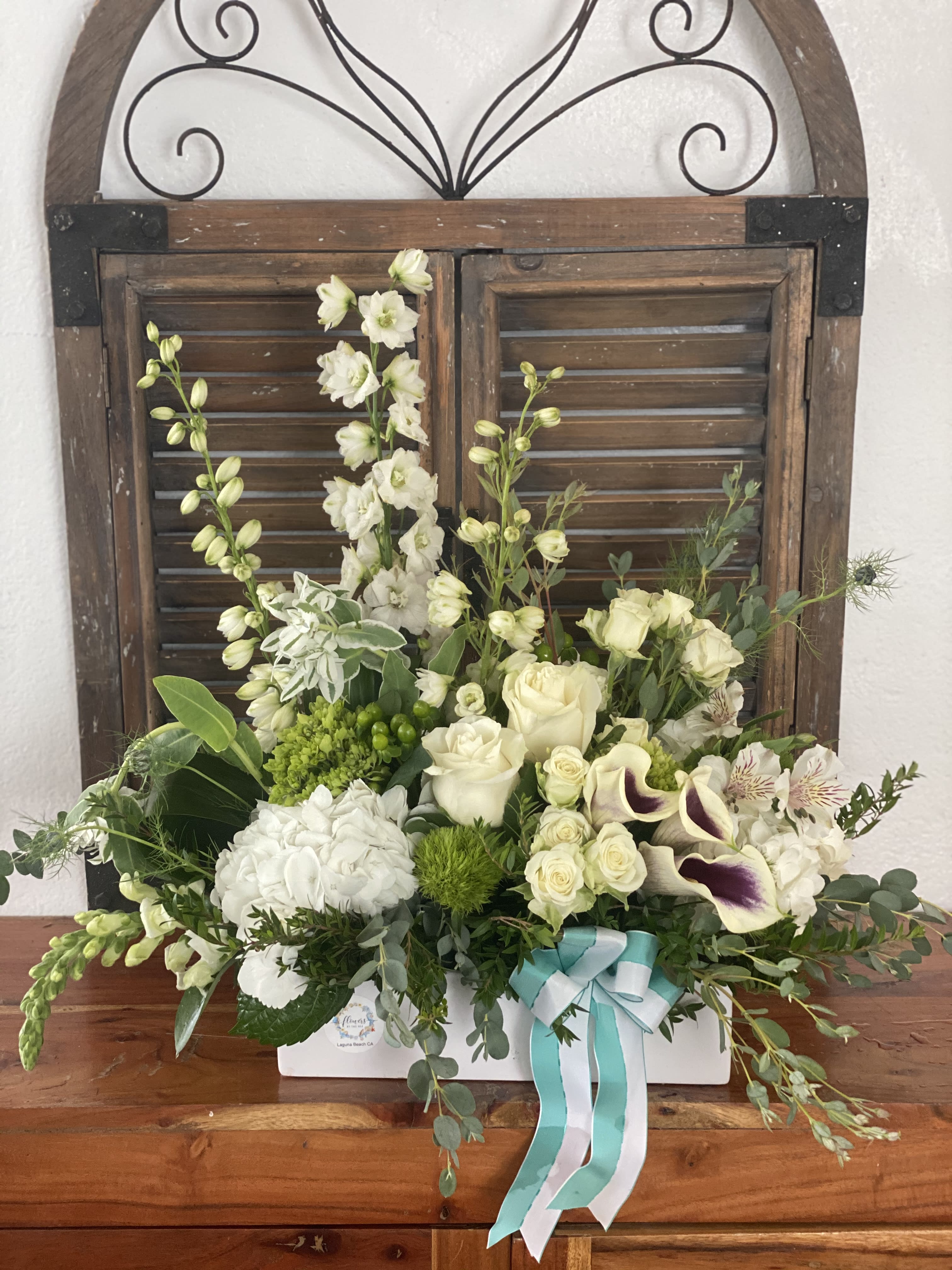 White floral arrangement in a white box with a teal ribbon