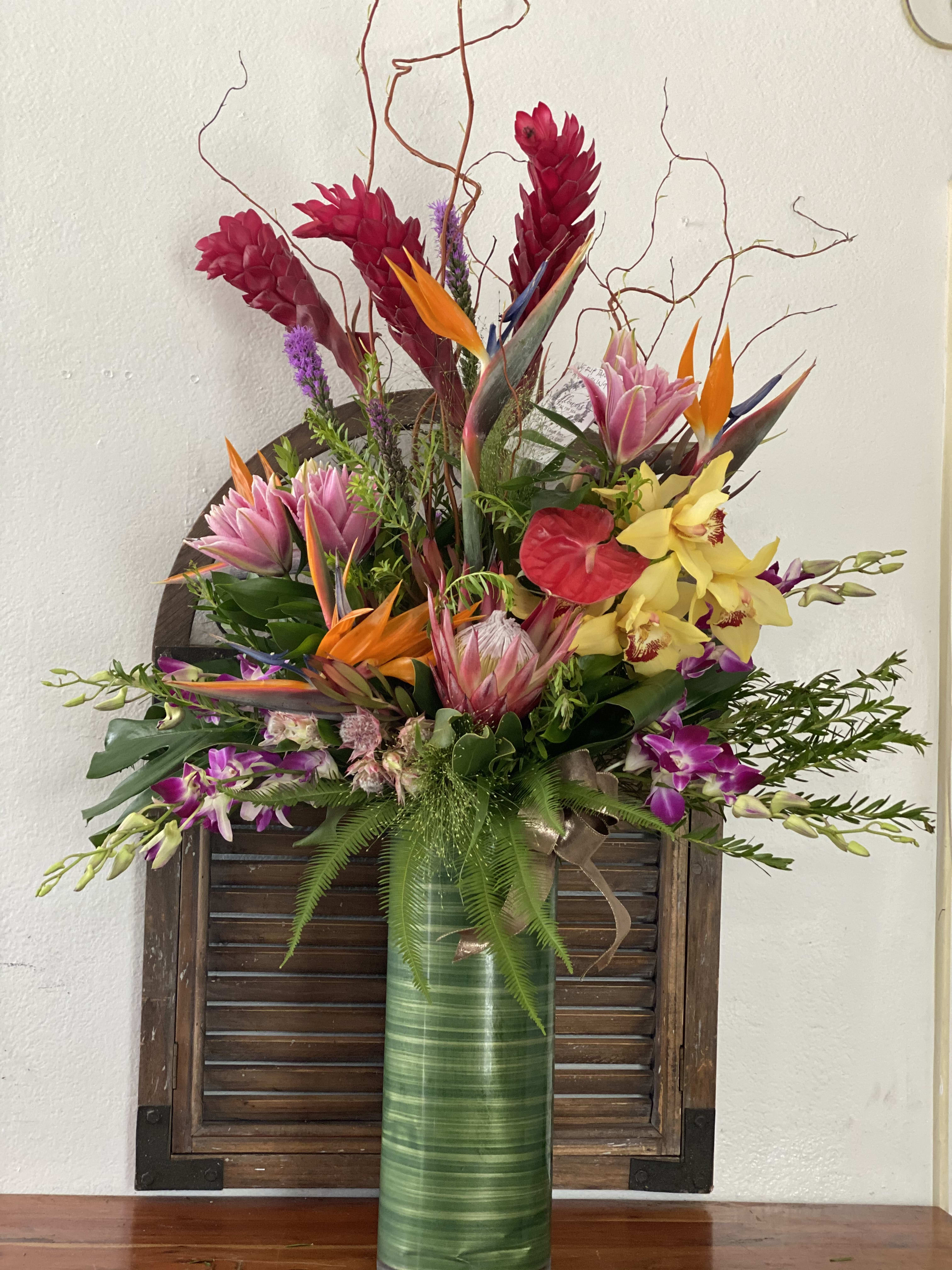 Tropical flower arrangement in a tall green vase with orchids and bird-of-paradise