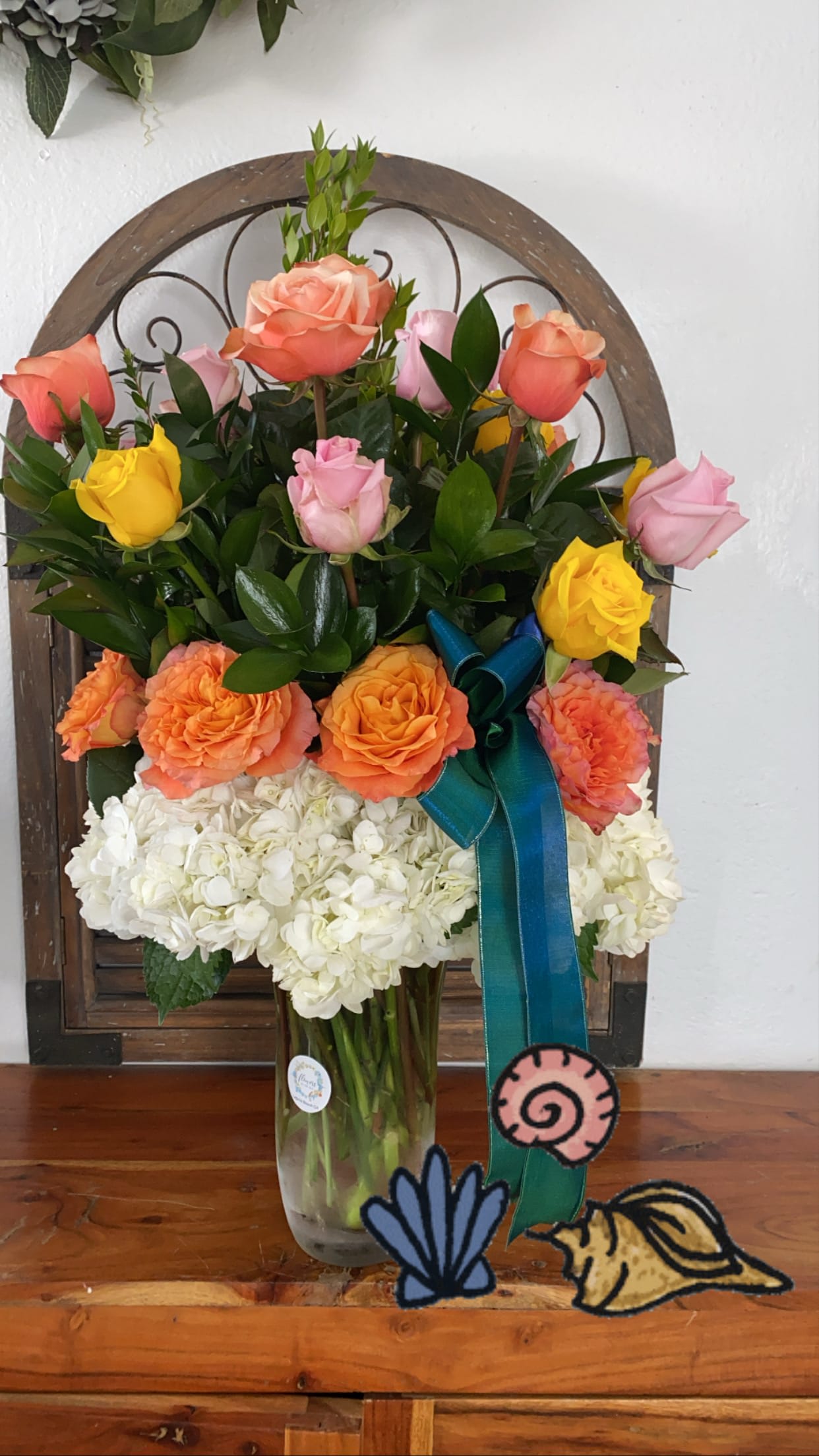 Mixed roses and white hydrangeas in a glass vase with a blue ribbon
