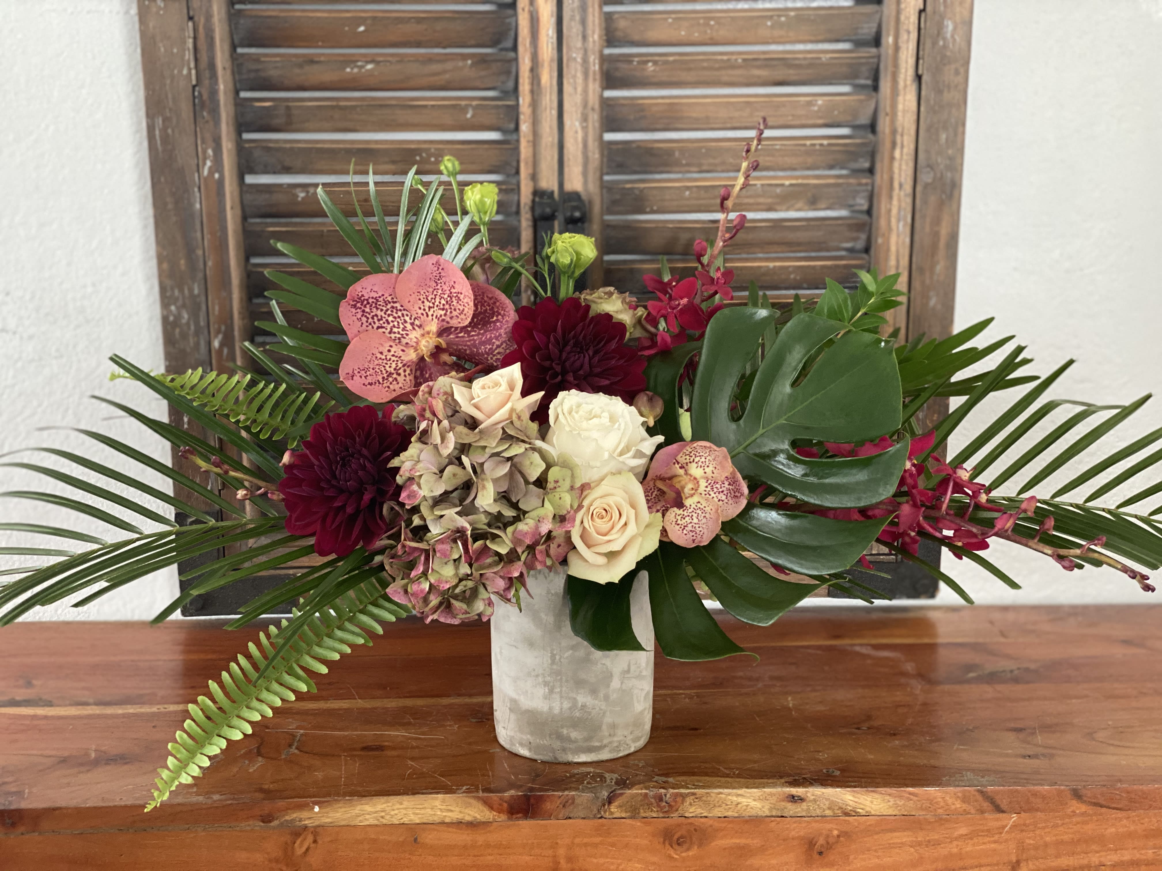 Tropical bouquet with orchids, roses, and dark dahlias in a white vase