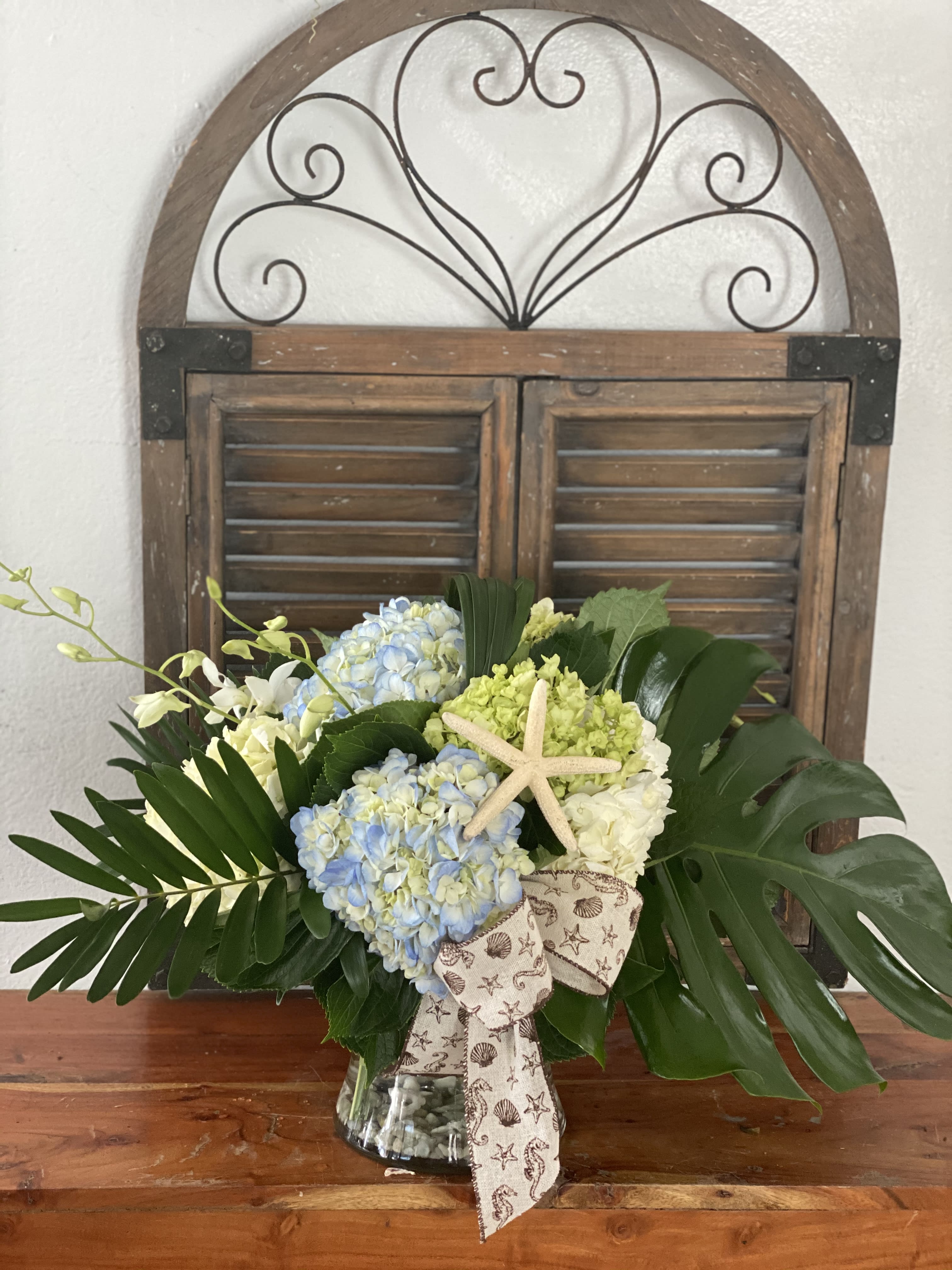 Hydrangea arrangement in a glass vase with a starfish accent and ribbon