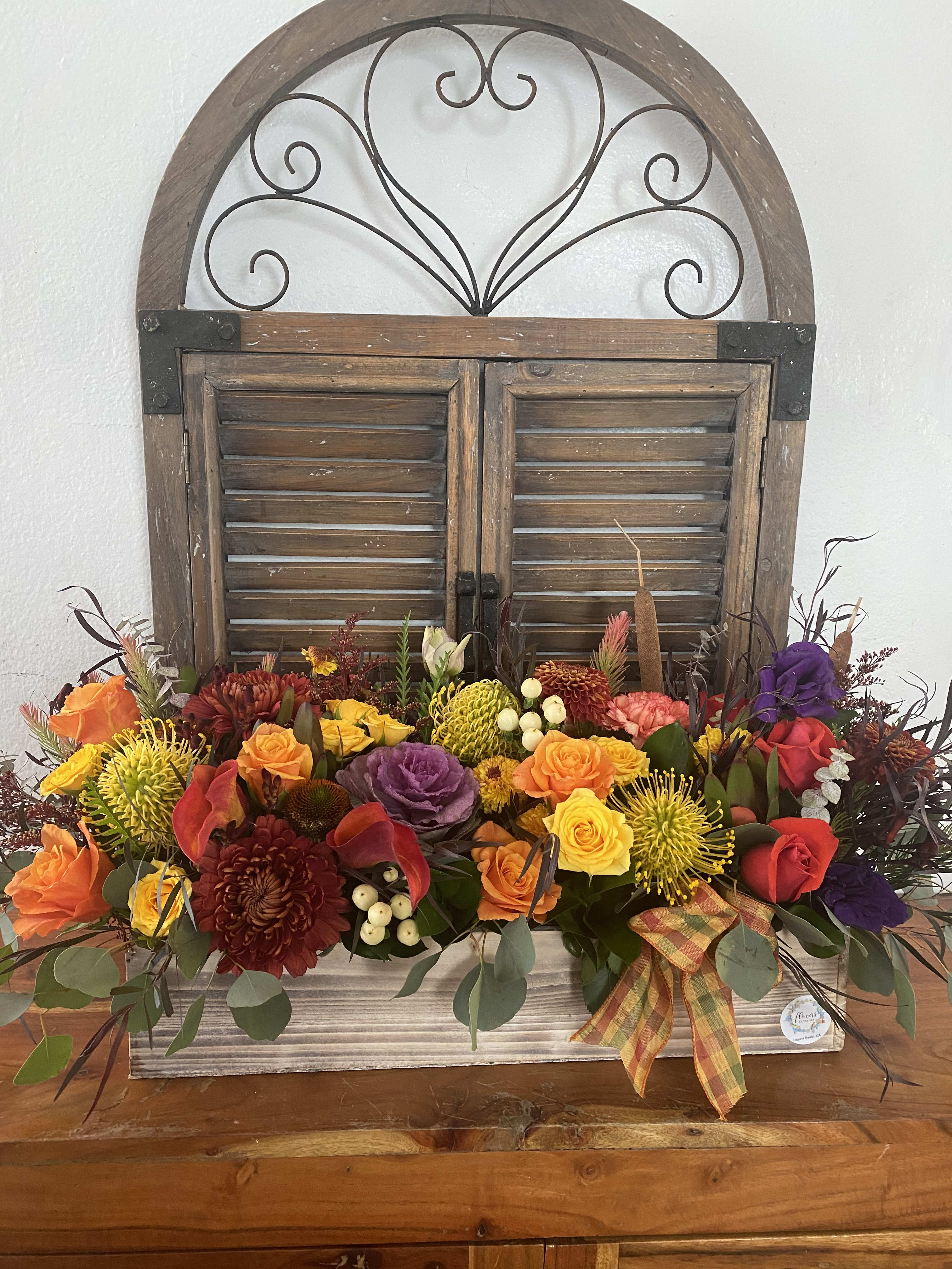 Colorful mixed flower arrangement in a wooden container with a plaid ribbon