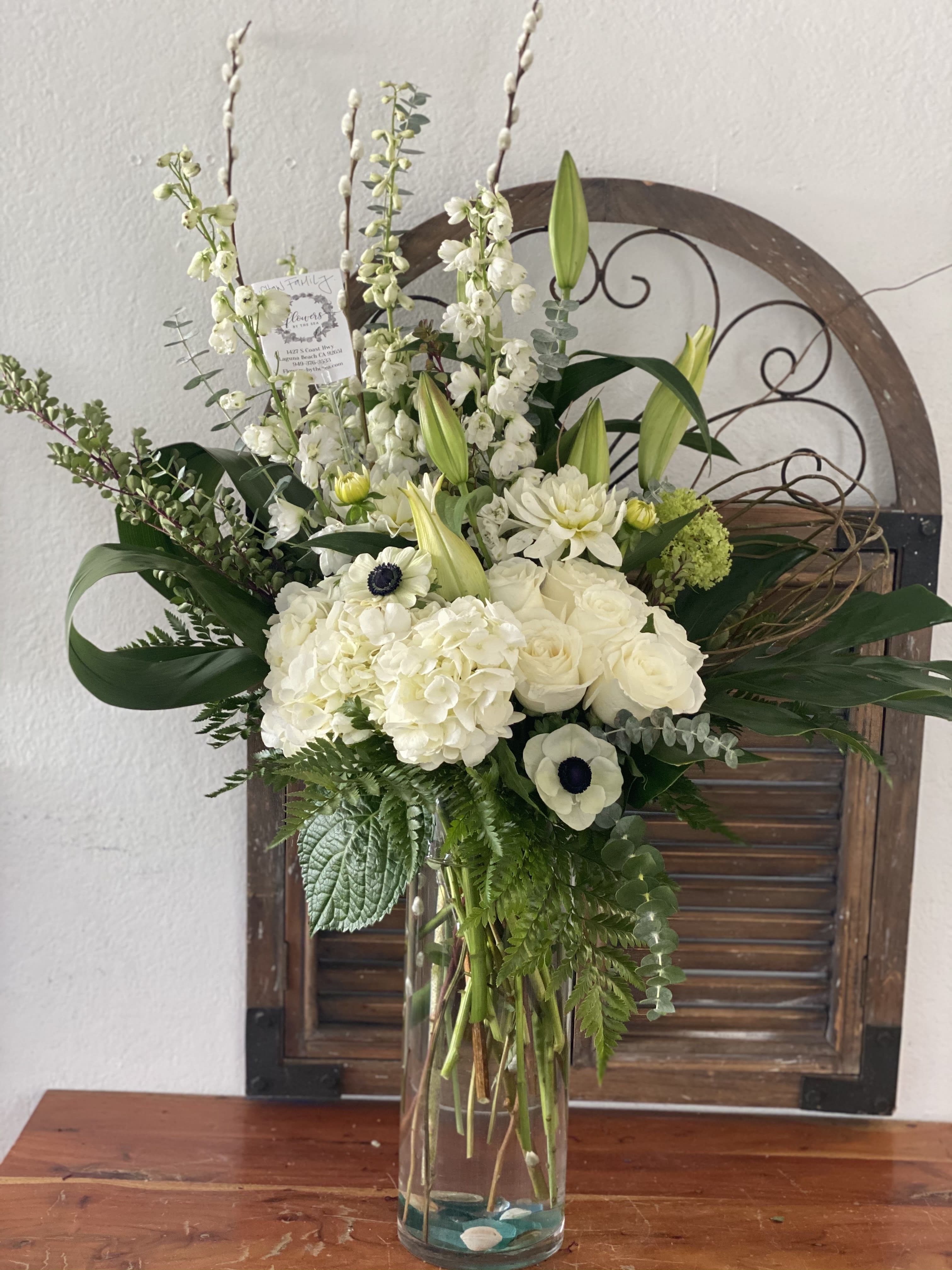 White floral arrangement in a clear glass vase with tall stems and greenery