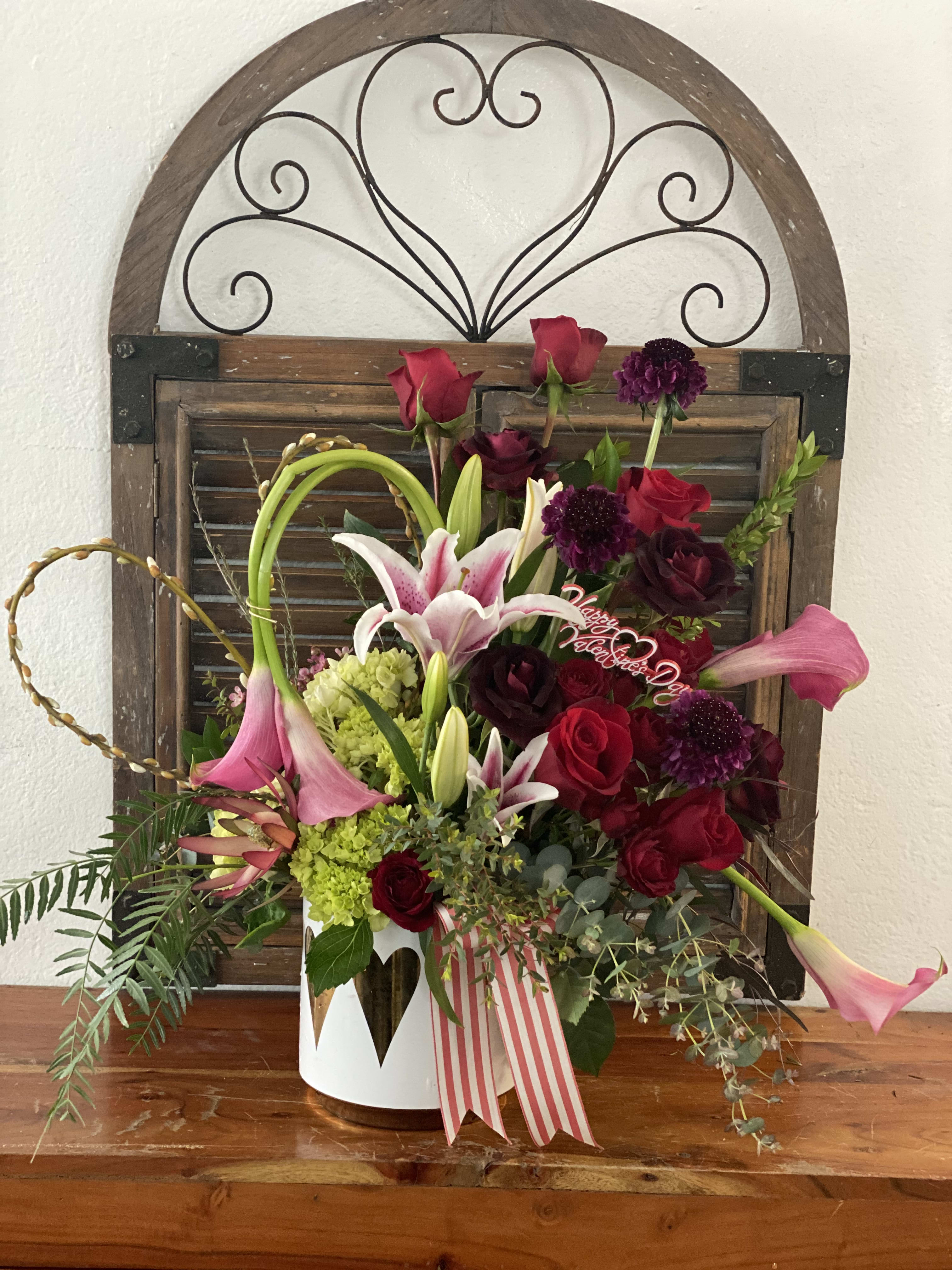 Mixed bouquet of red roses, pink lilies, and purple blooms in a white container