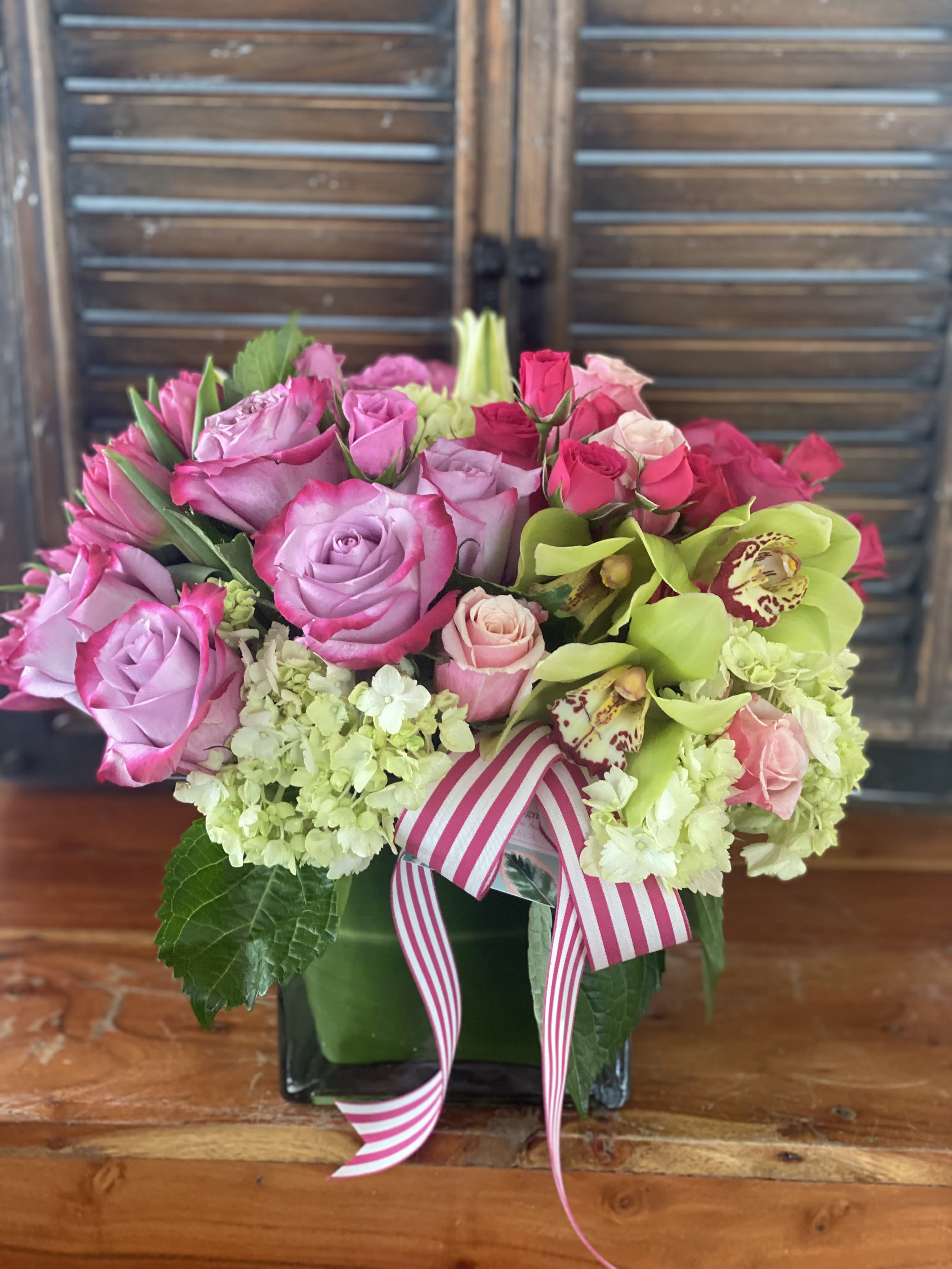 Pink and lavender roses with green orchids in a square vase