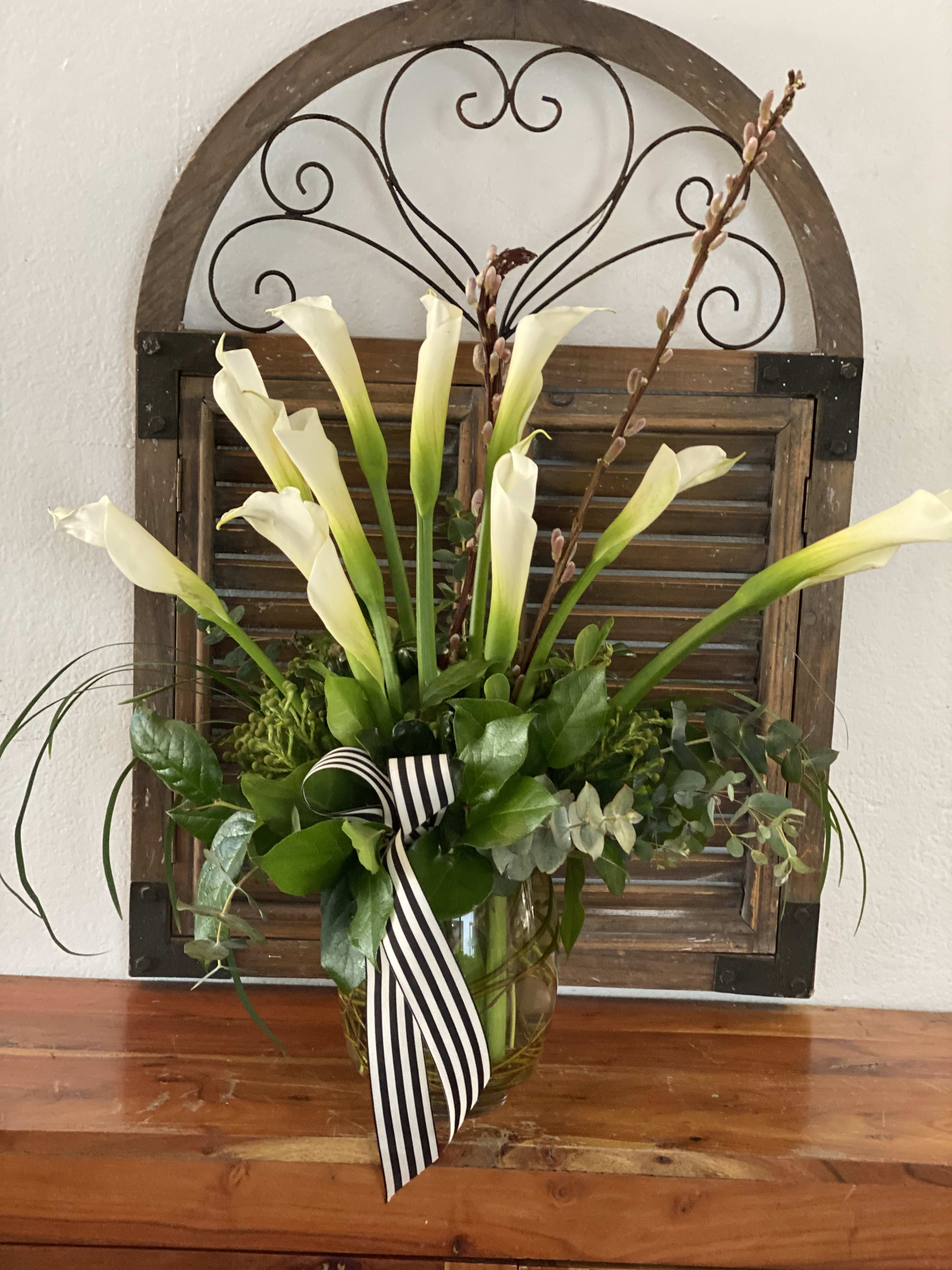 White calla lilies in a glass vase with a striped ribbon
