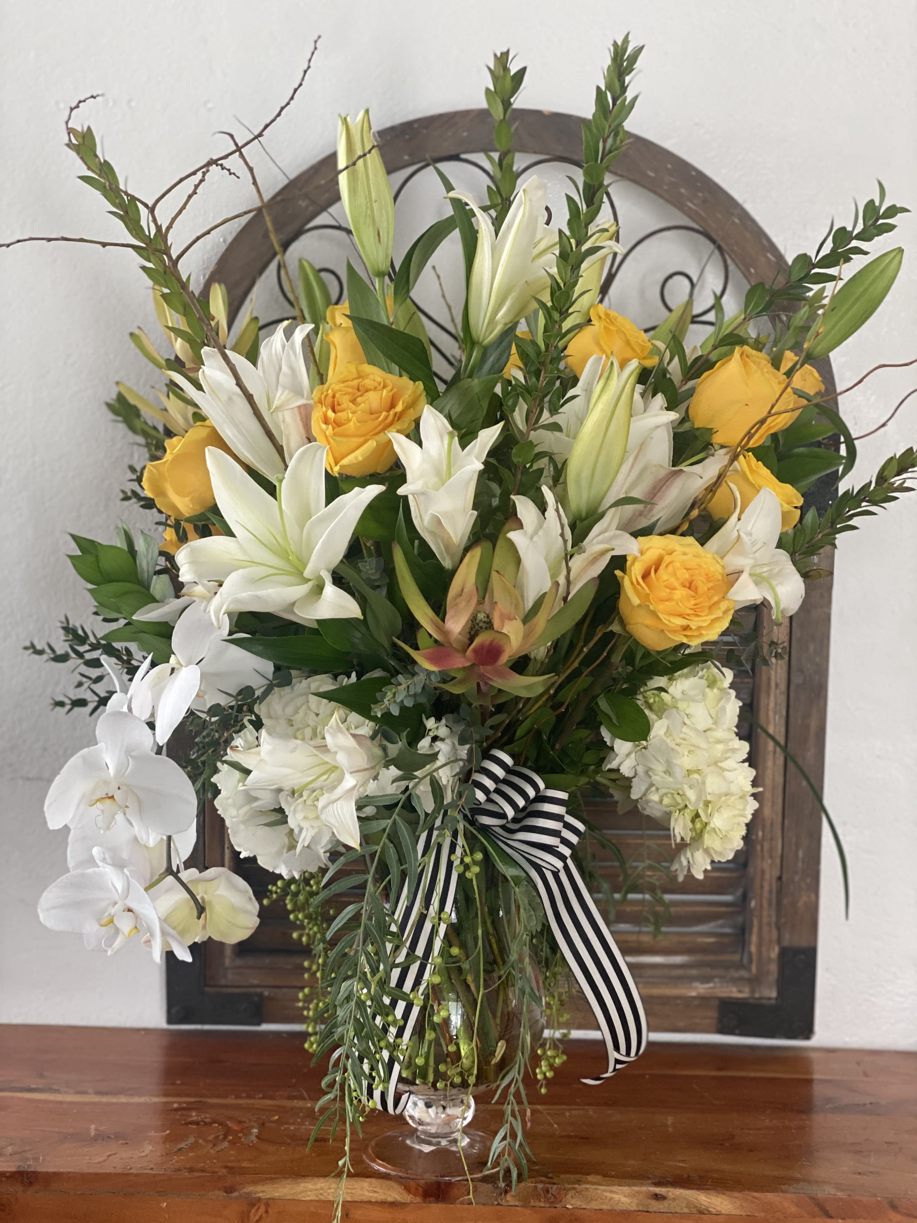 Yellow roses and white lilies in a glass vase with a striped ribbon