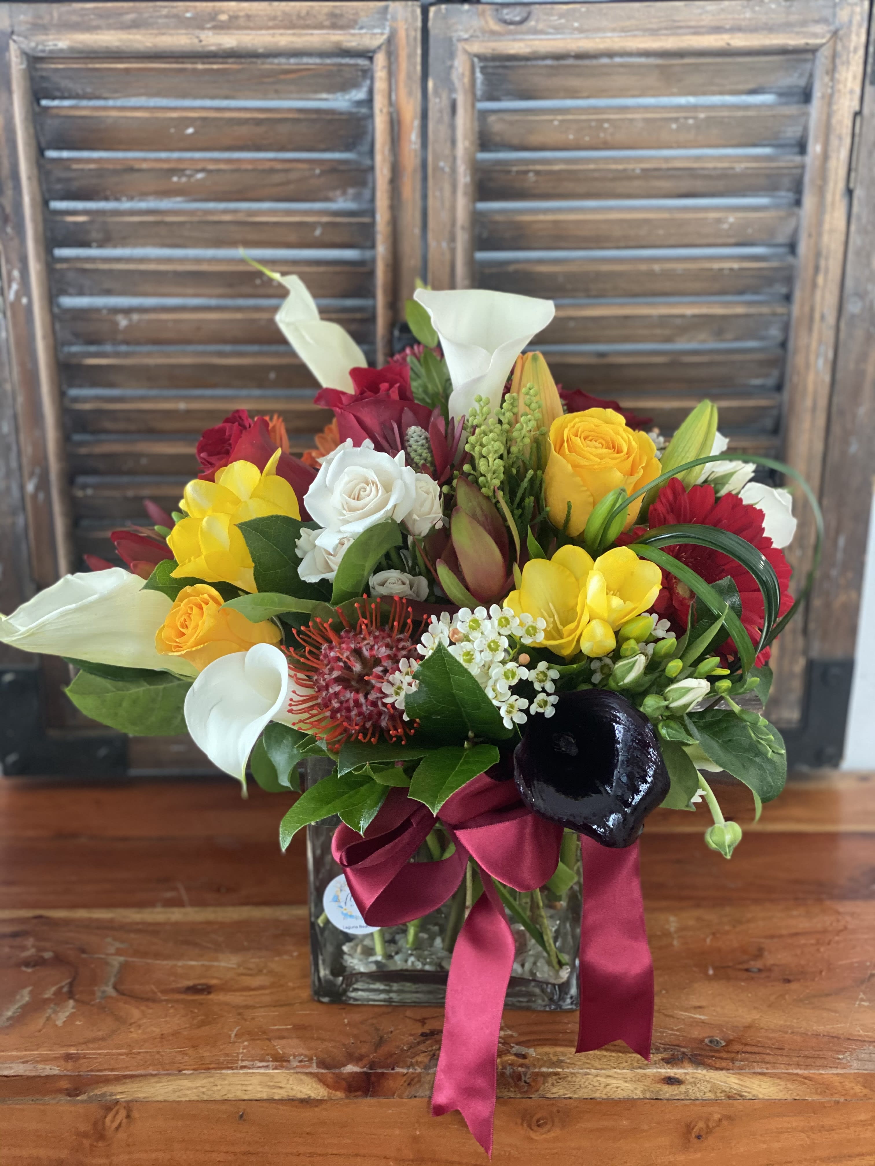 Mixed bouquet in a glass vase with white calla lilies, roses, and bright yellow blooms