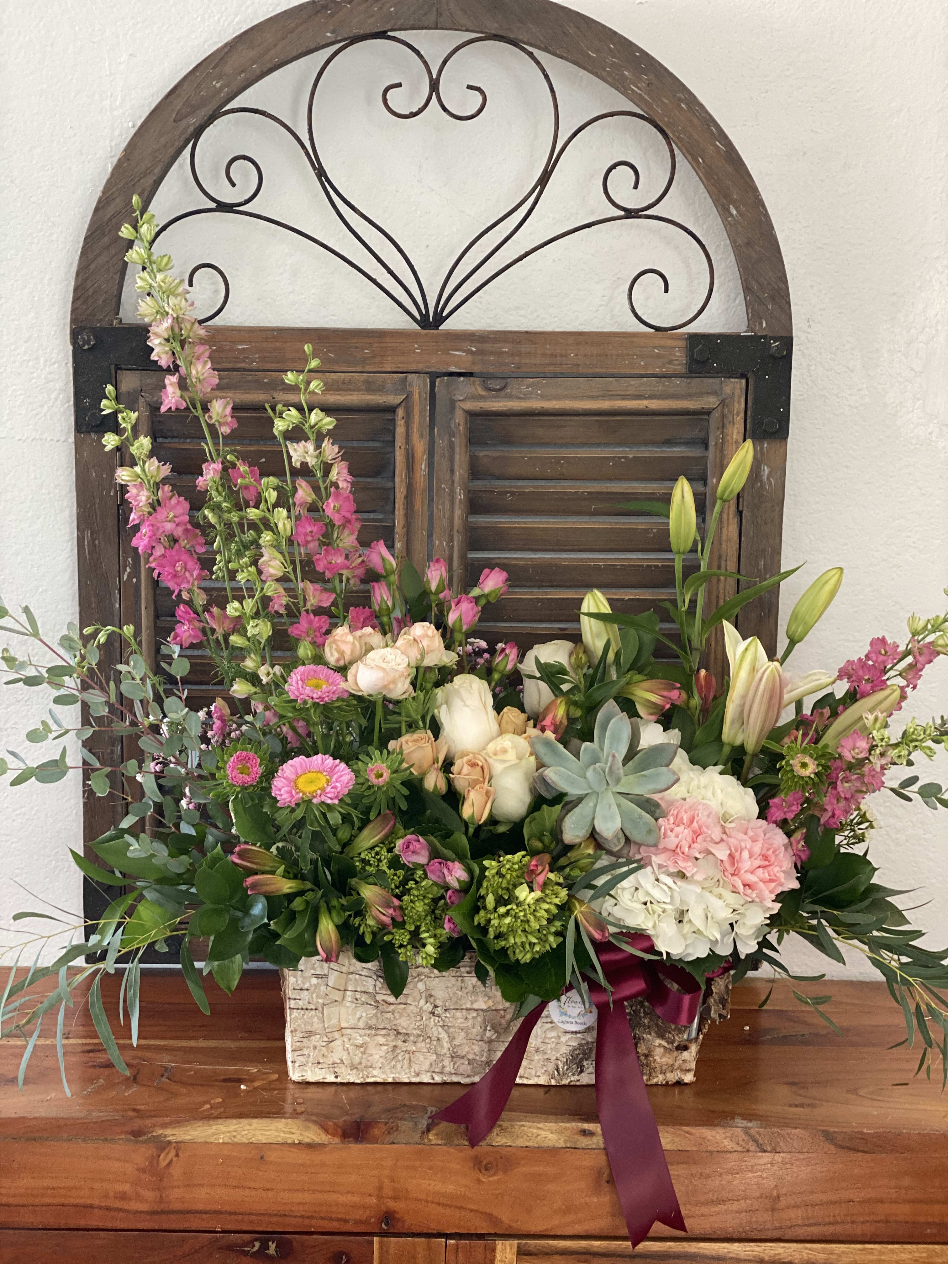 Mixed floral arrangement in a rustic rectangular container with pink and white blooms